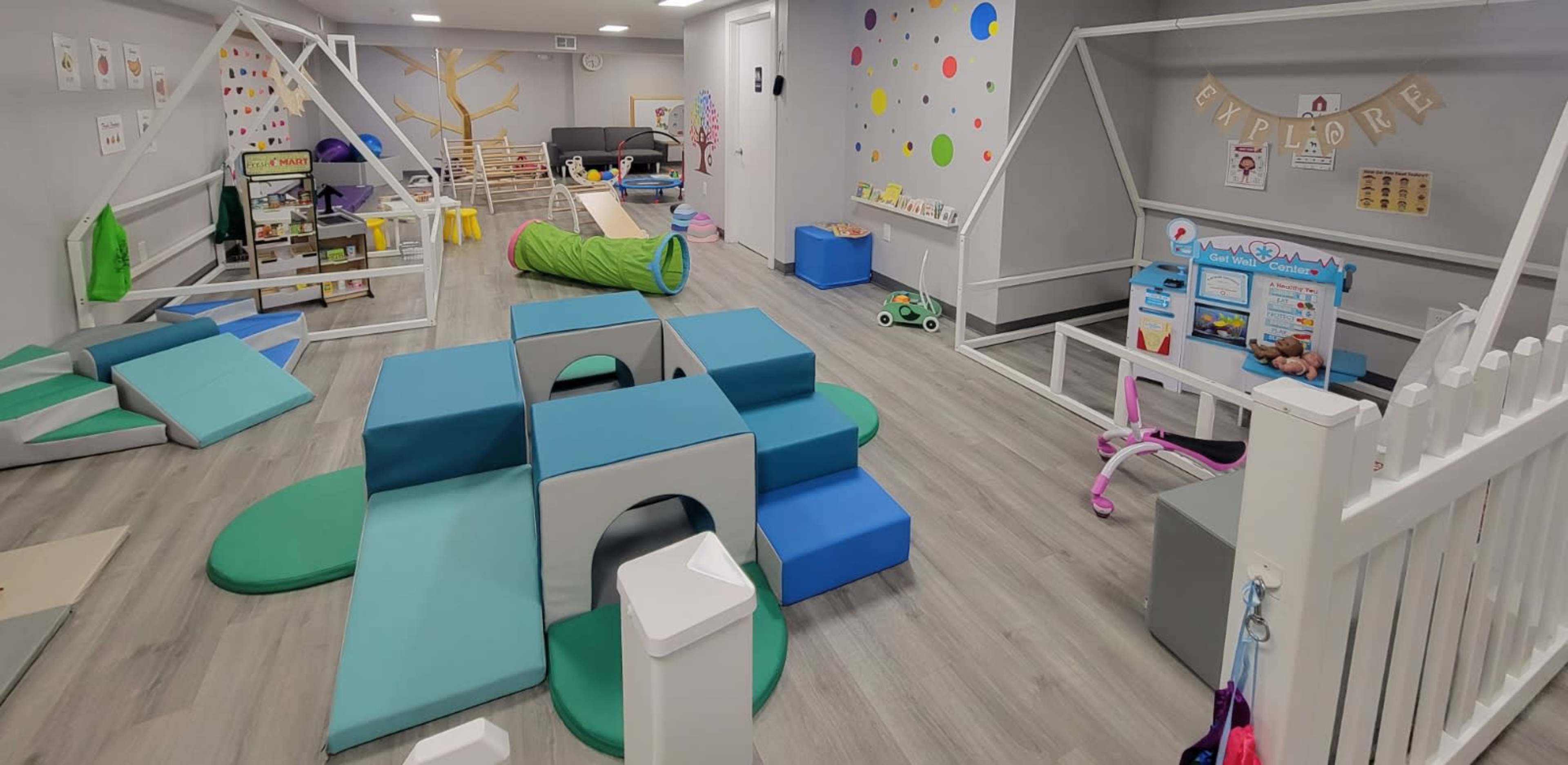 A brightly colored playroom with various soft play structures, a tunnel, and activity areas for children.