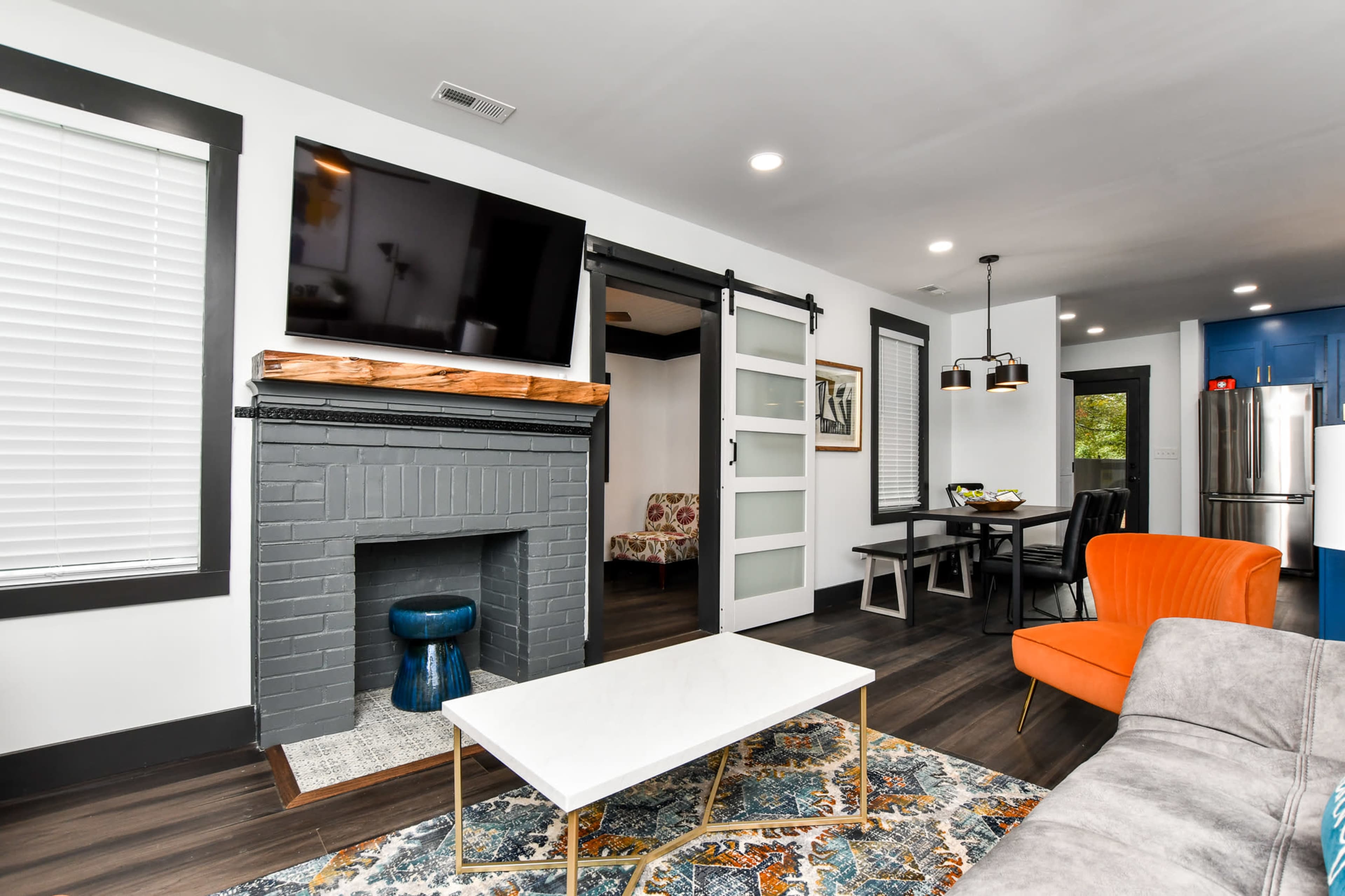 A modern living room with a fireplace, a large wall-mounted TV, a coffee table, and an orange armchair.