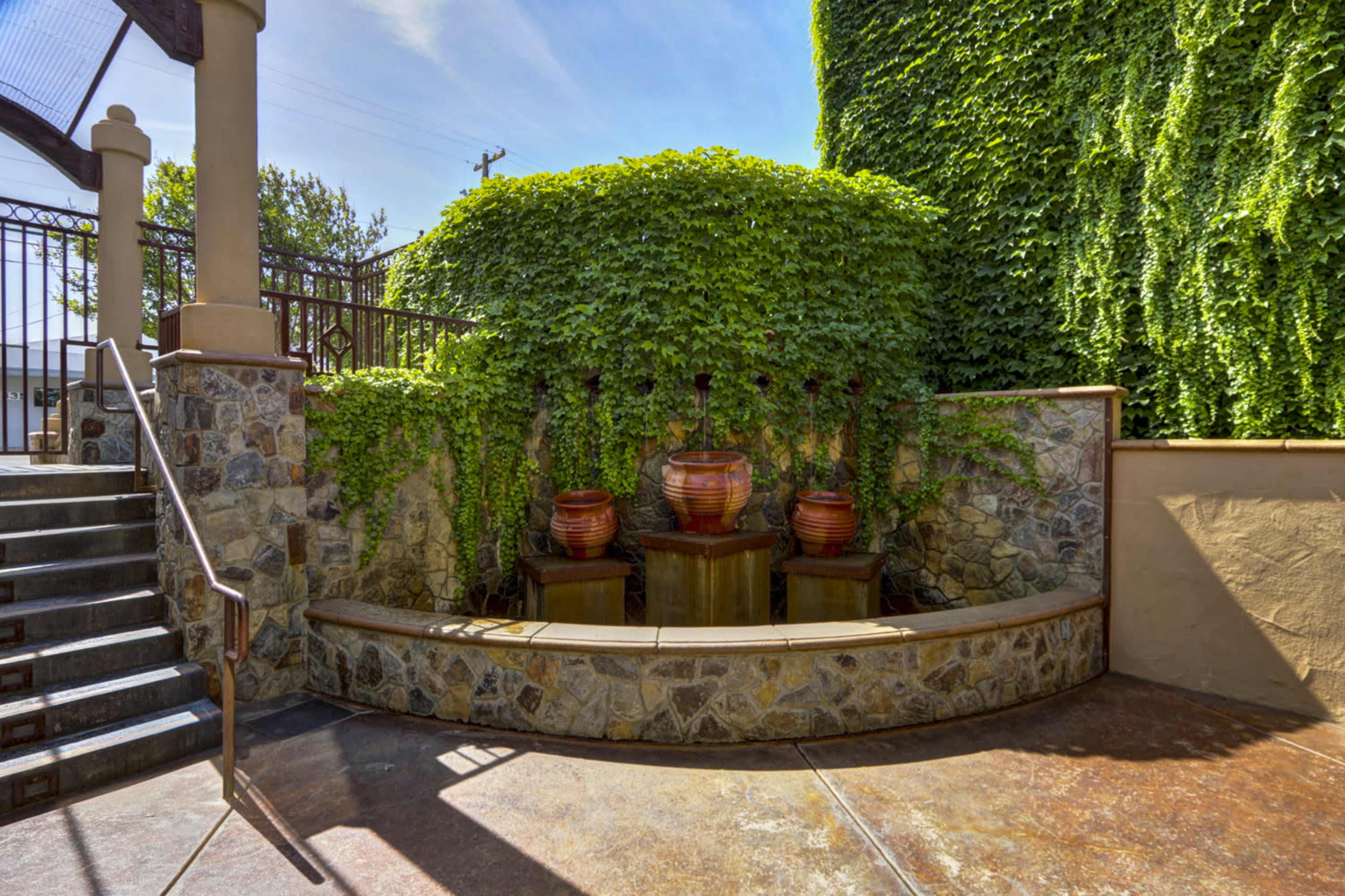 A small outdoor area featuring a stone wall with three water fountains and lush green ivy cascading over the top.