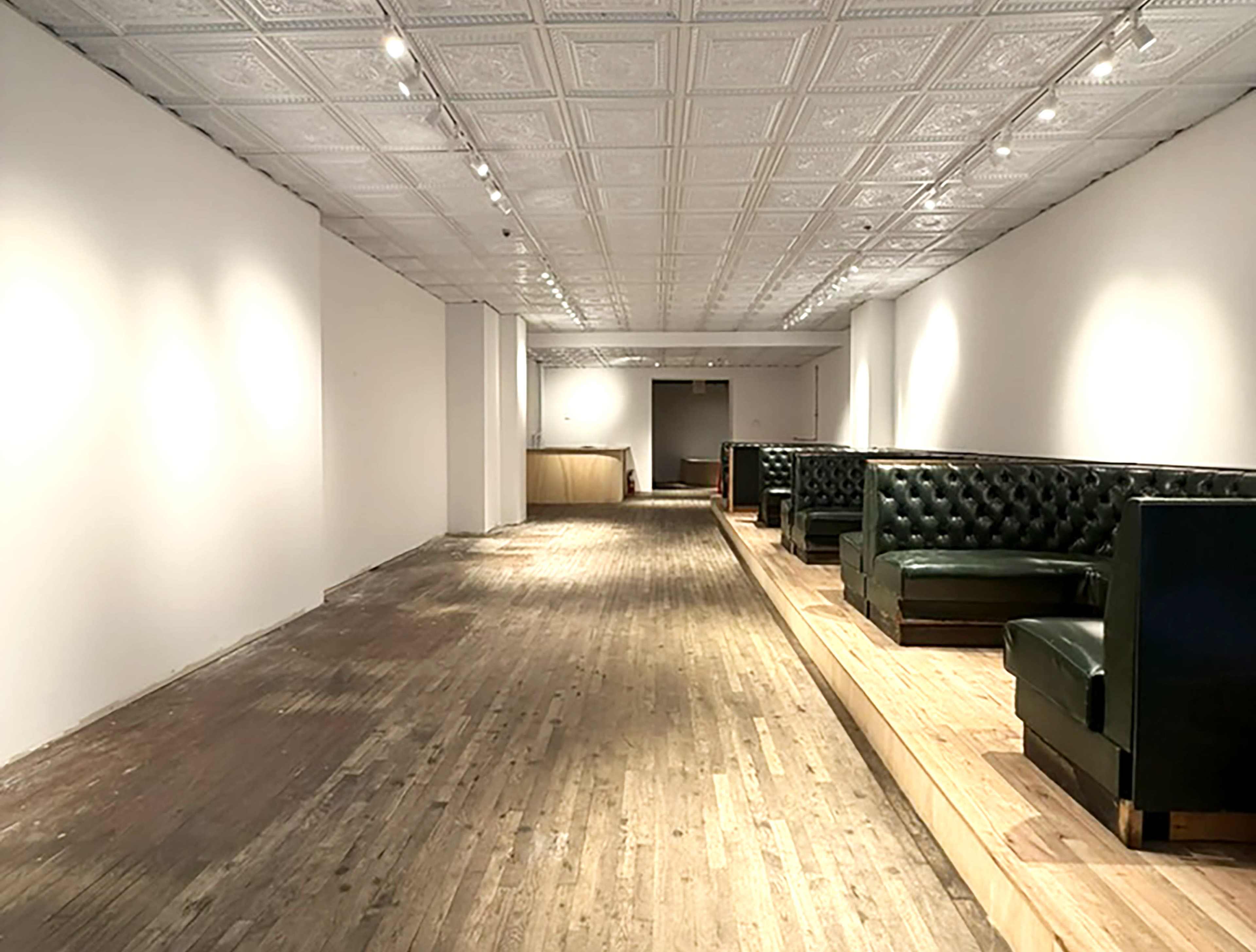 The image shows a long, narrow interior space with wooden floors, empty booths along the walls, and a coffered ceiling.