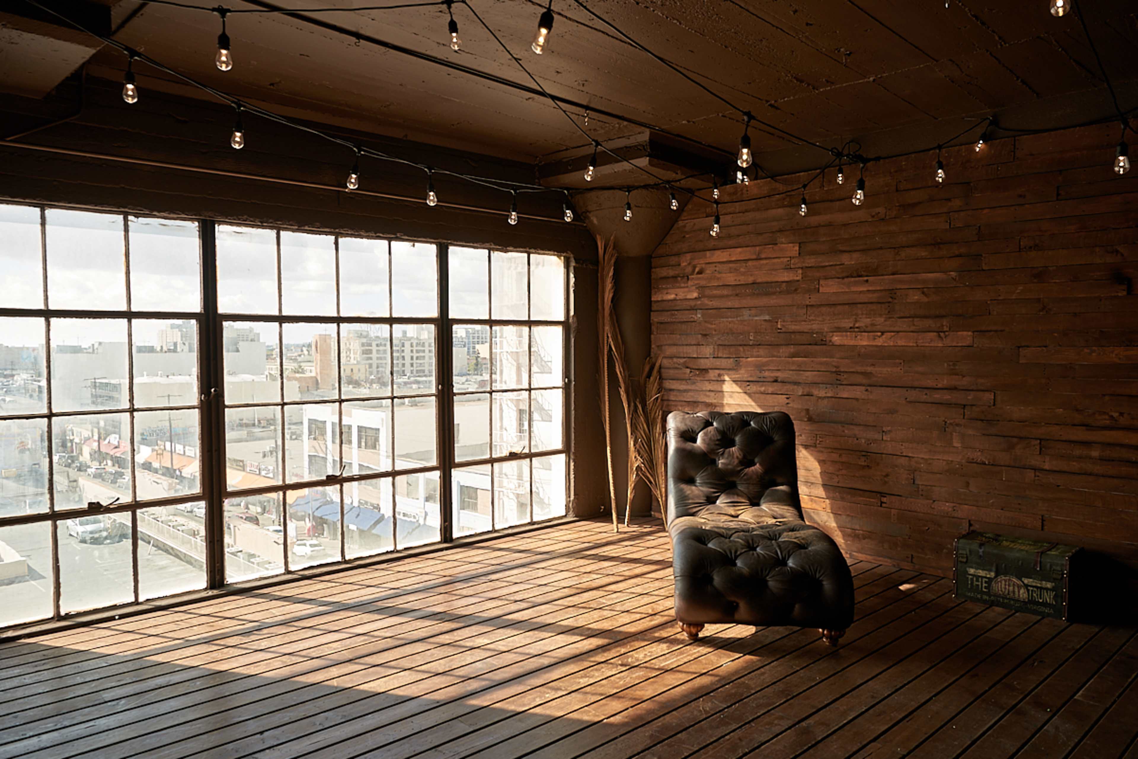 A rustic room with wooden walls, a large window overlooking a cityscape, and a vintage tufted leather chaise lounge.