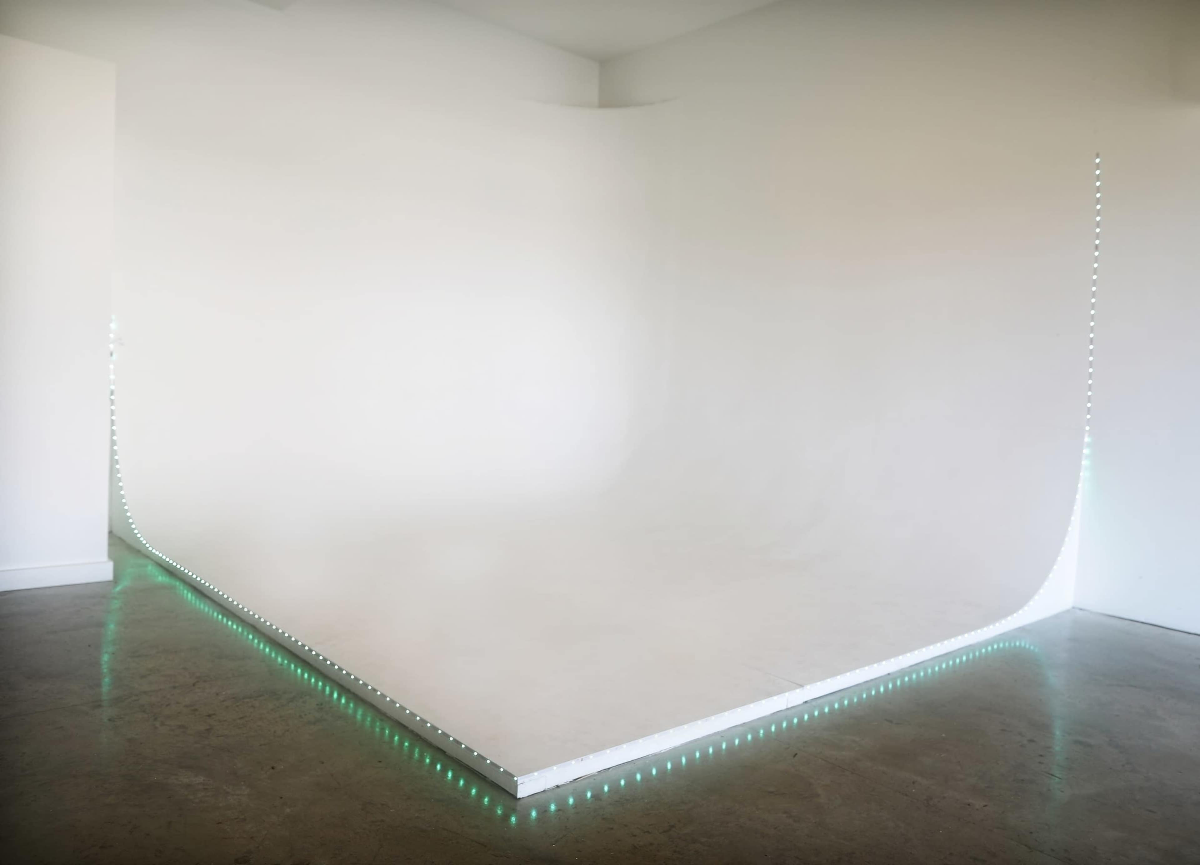 A minimalist interior space featuring a curved white backdrop with green LED lights along the base.