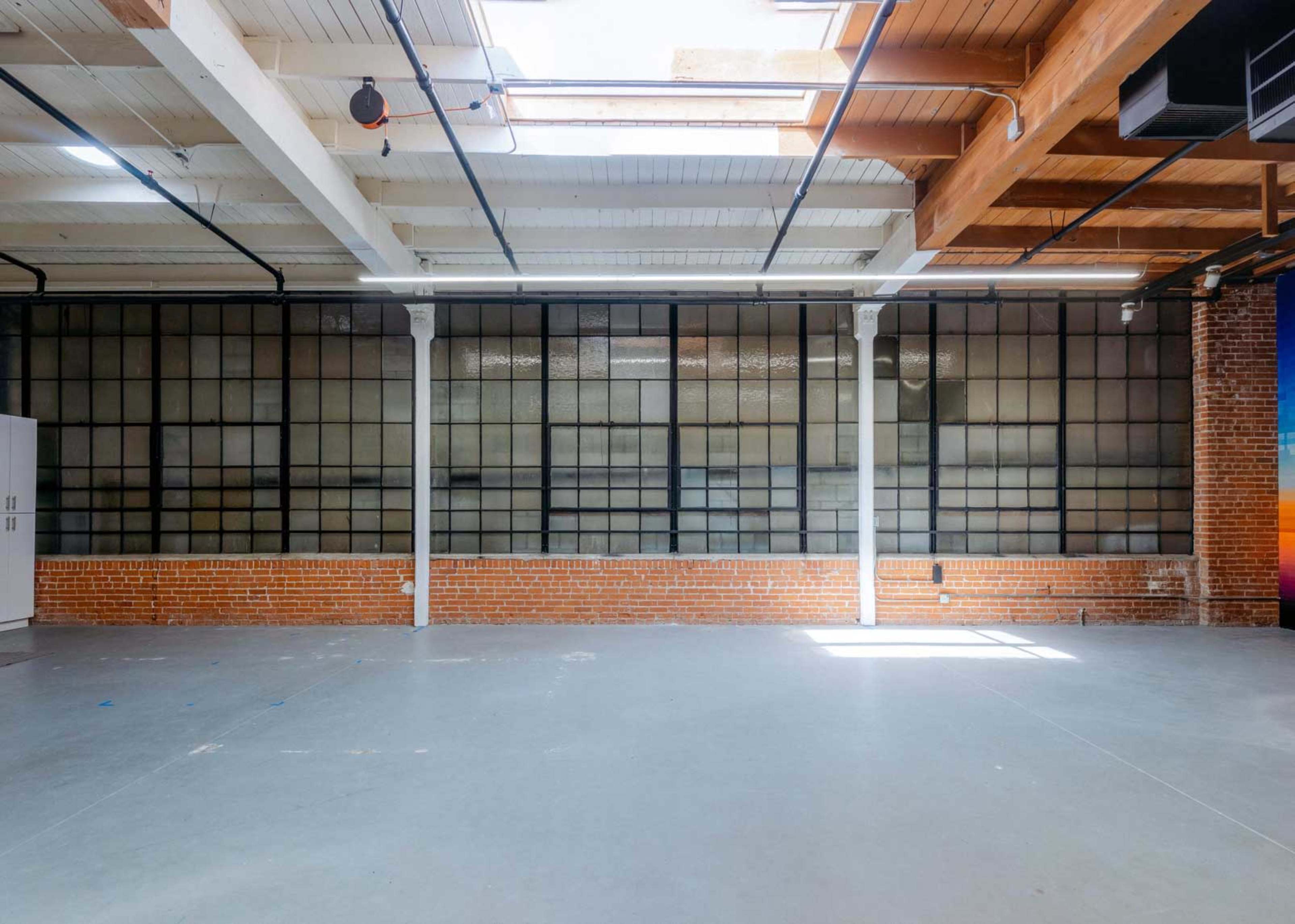A spacious industrial room features large glass-paneled windows and exposed brick walls.