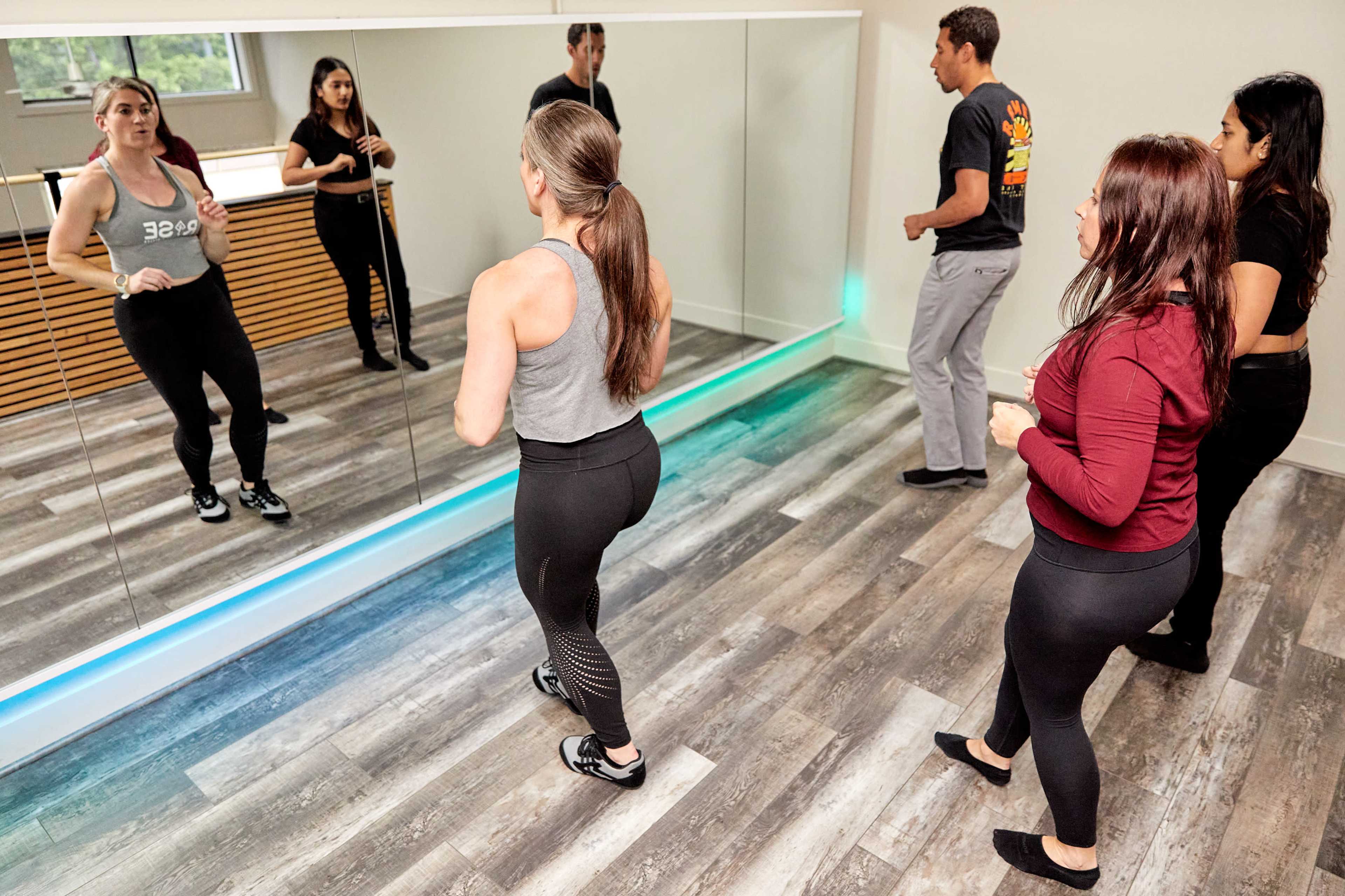 Four individuals are practicing dance moves in front of a mirror in a spacious studio.