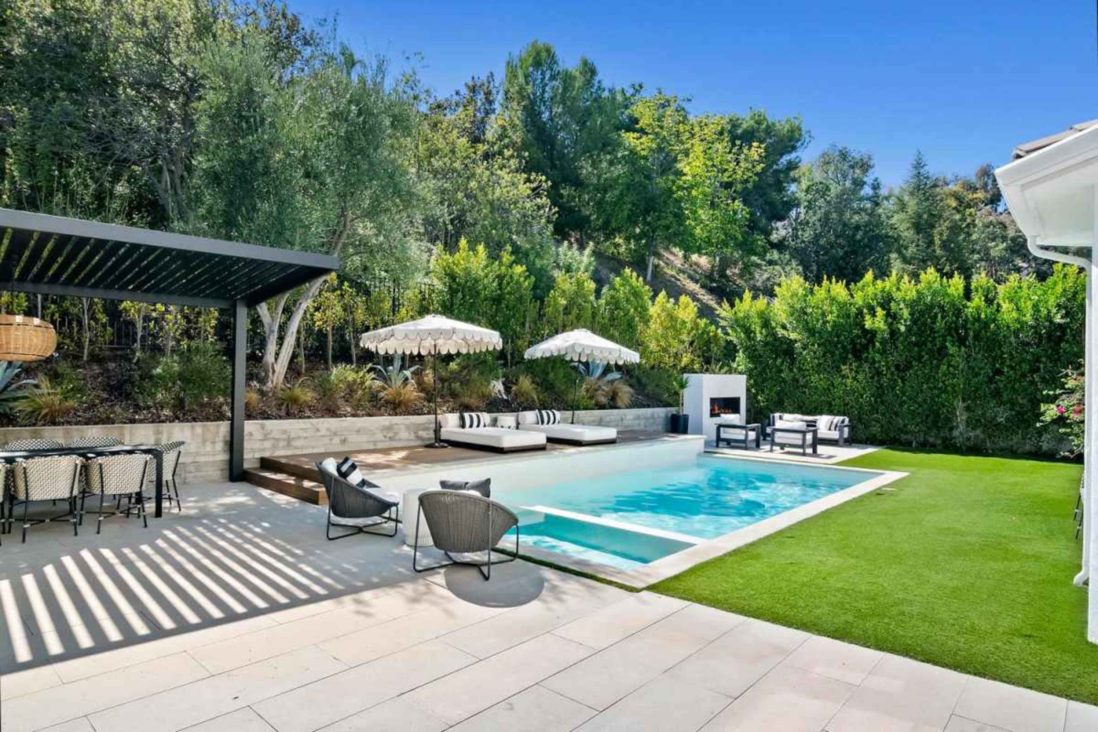 The image features a modern outdoor pool area with a rectangular pool, lounge chairs under umbrellas, and a dining set on a patio surrounded by greenery.
