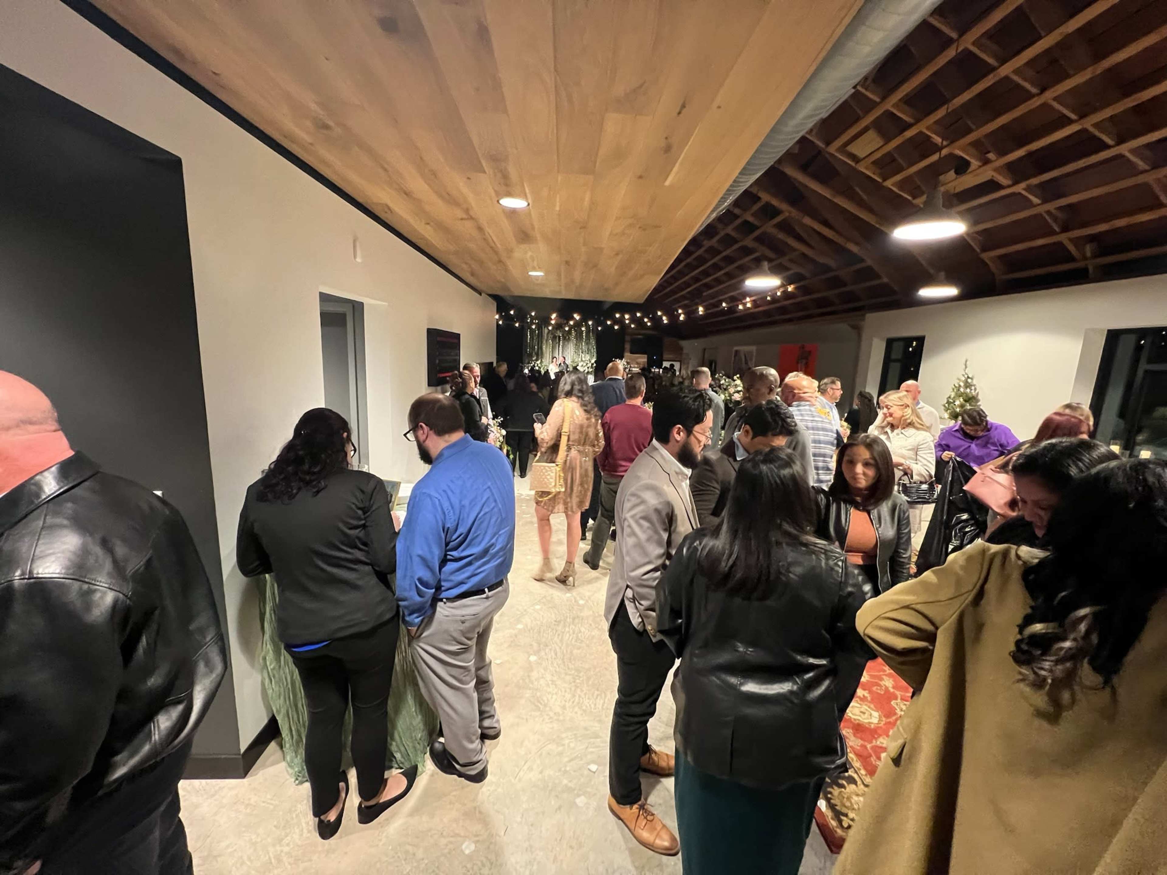 A large group of people mingles in a well-lit hallway adorned with wooden beams and modern decor during an indoor event.