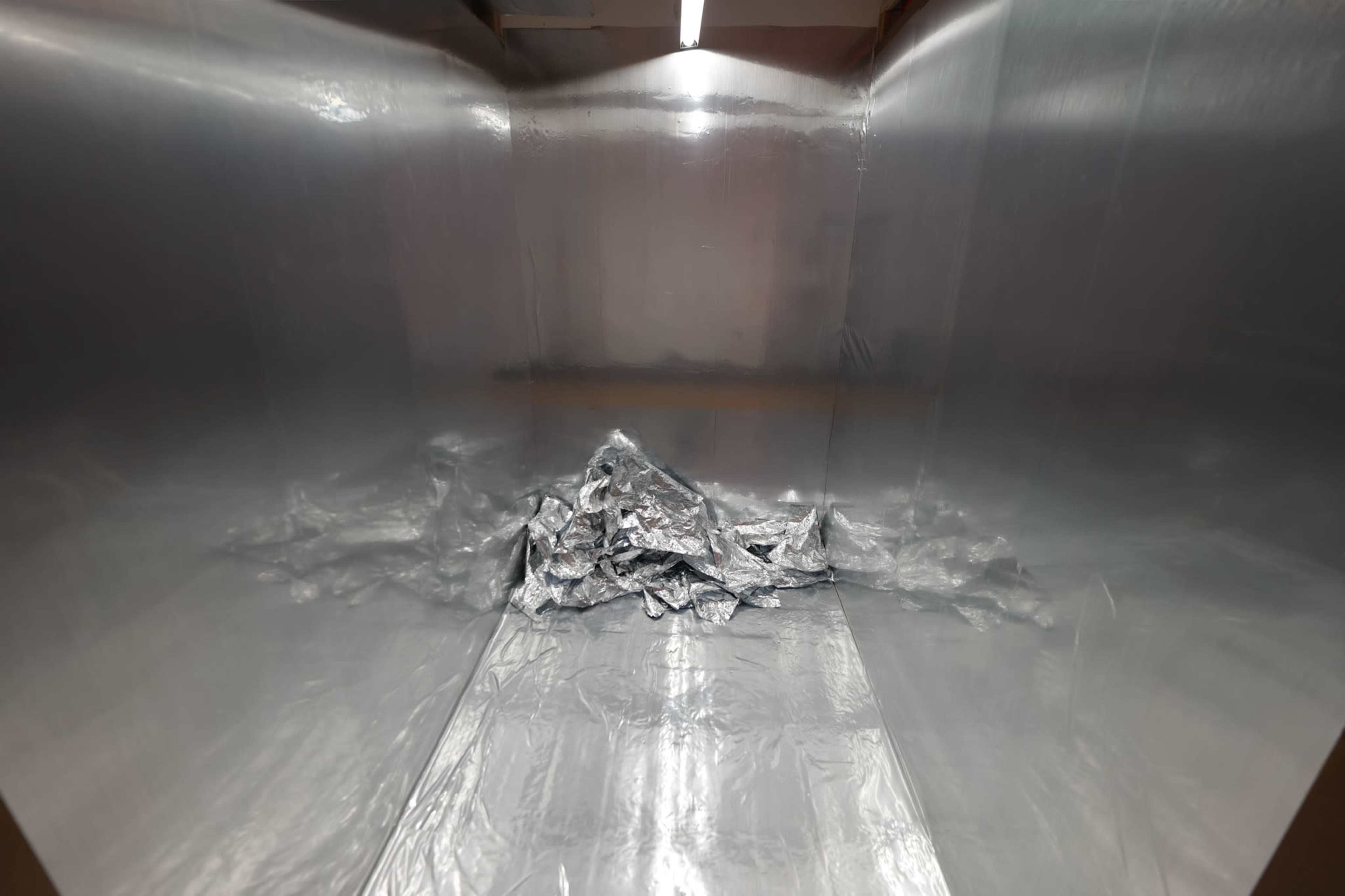 The image shows a reflective, metallic interior space with a crumpled mass of silver material in the center.