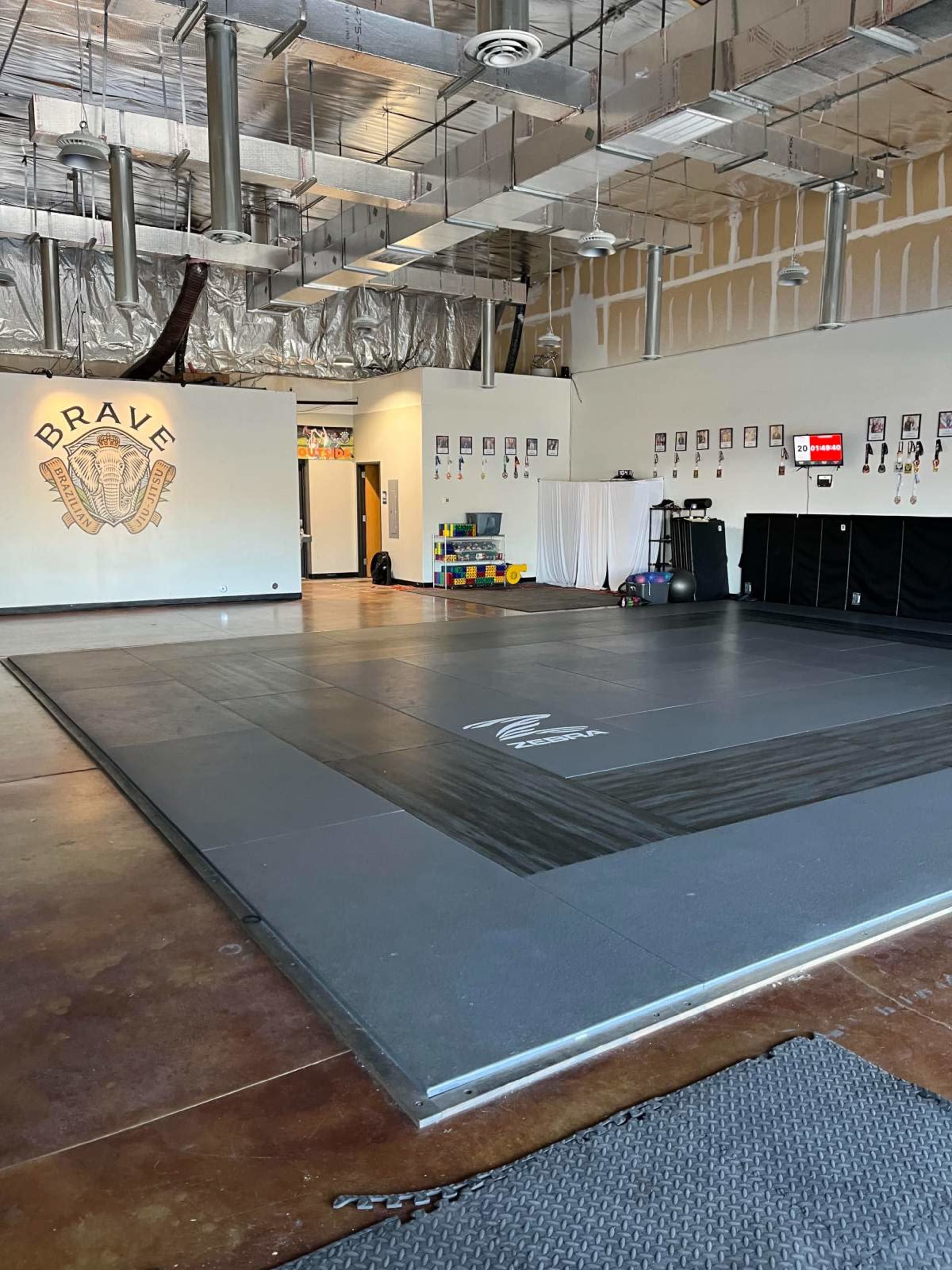 The image shows a spacious training room with a large, padded mat area and walls decorated with framed photographs.