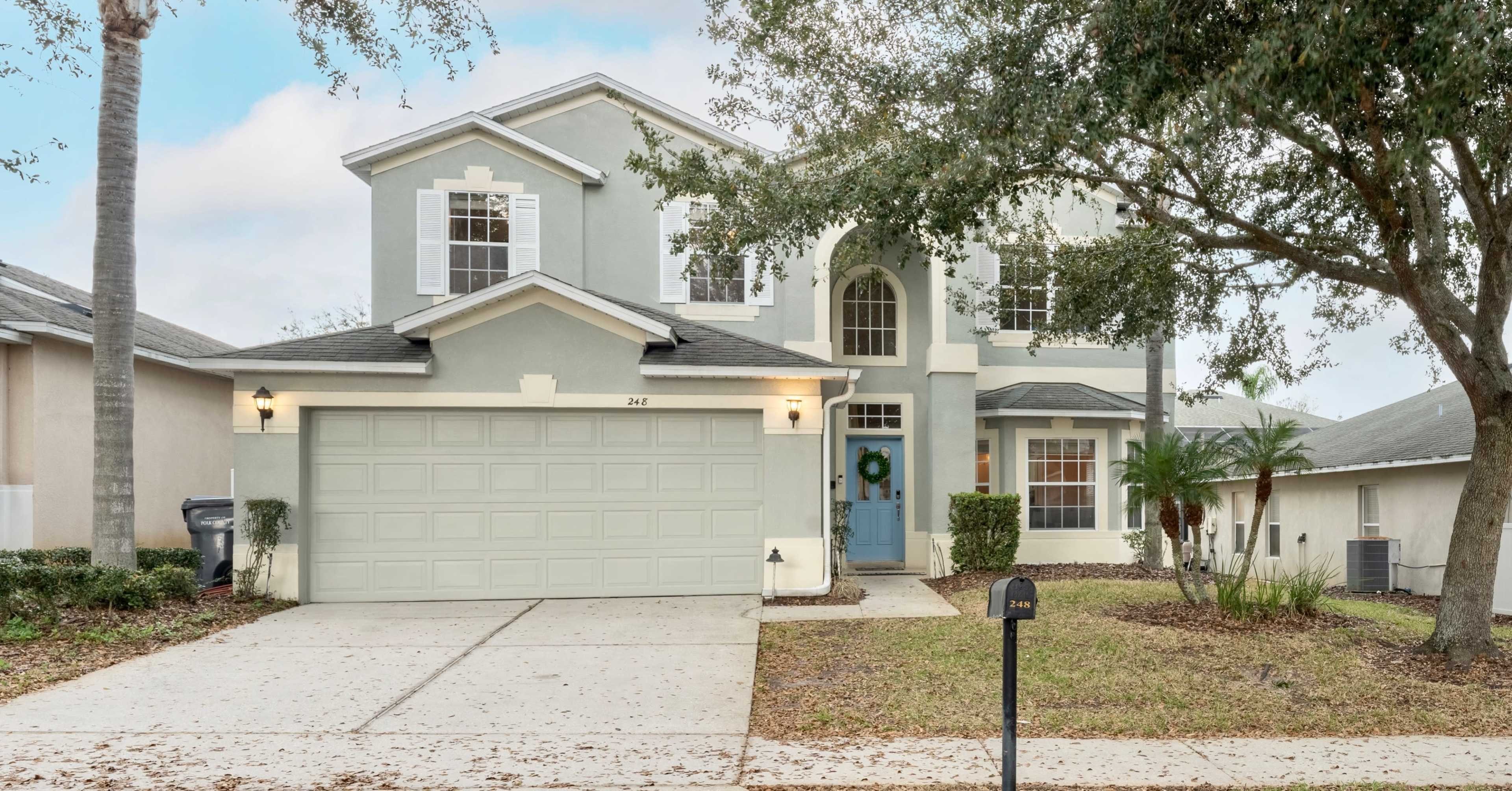 A two-story, light blue house with a two-car garage and a well-maintained front lawn.