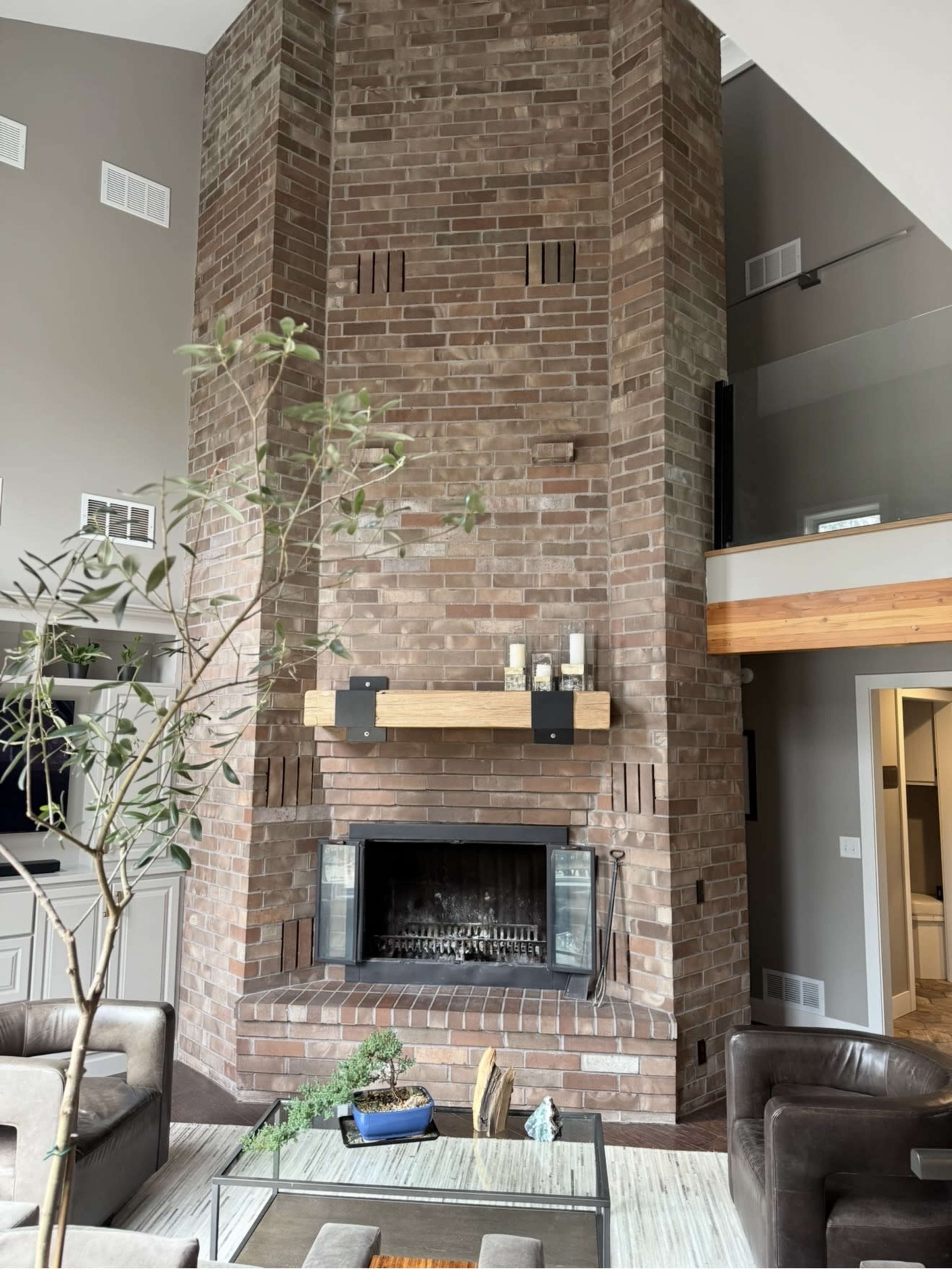 The image shows a modern living room with a large brick fireplace as the focal point, surrounded by neutral-colored walls and furniture.