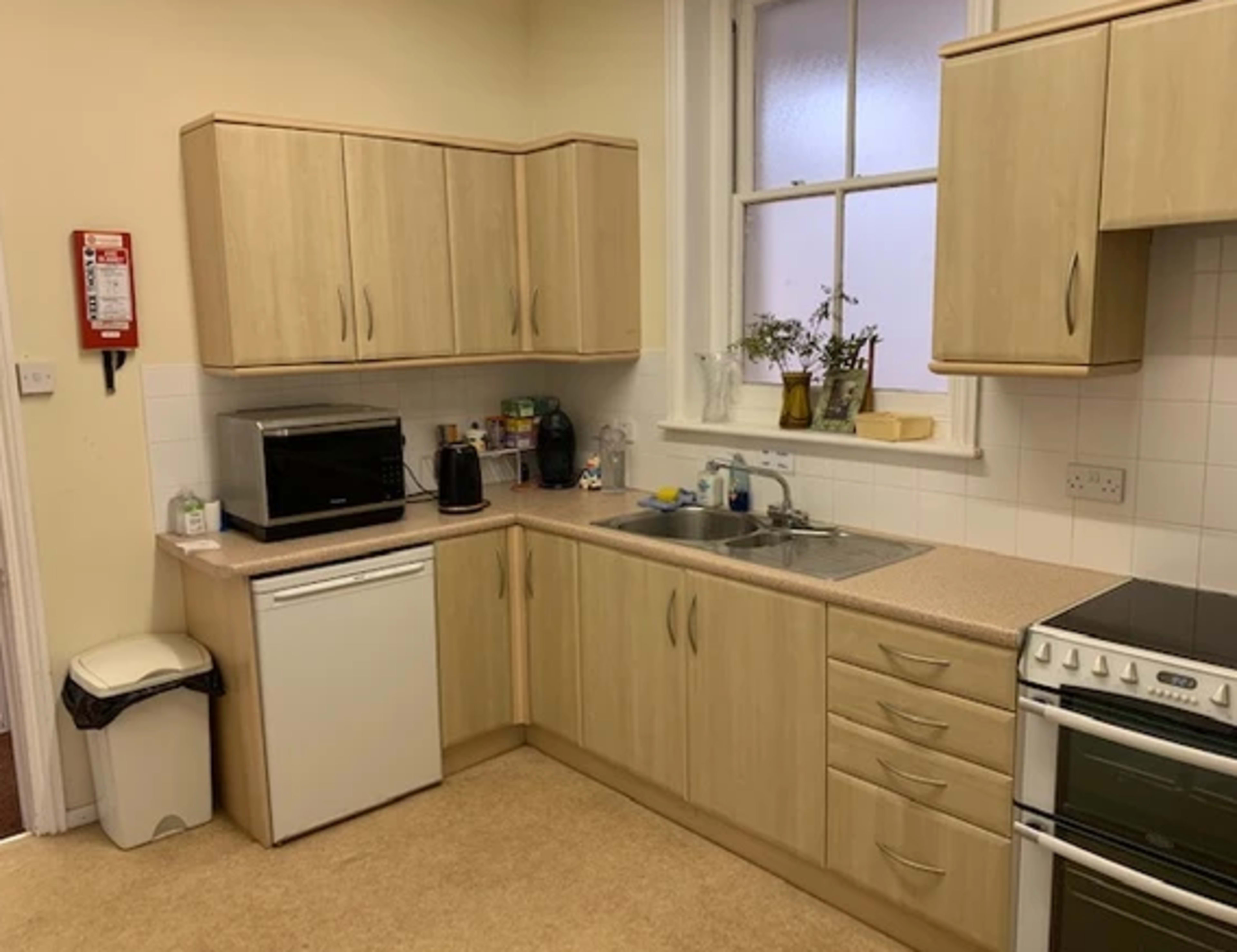 A kitchen with wooden cabinets, a sink, a microwave, a kettle, a dishwasher, and a stove.