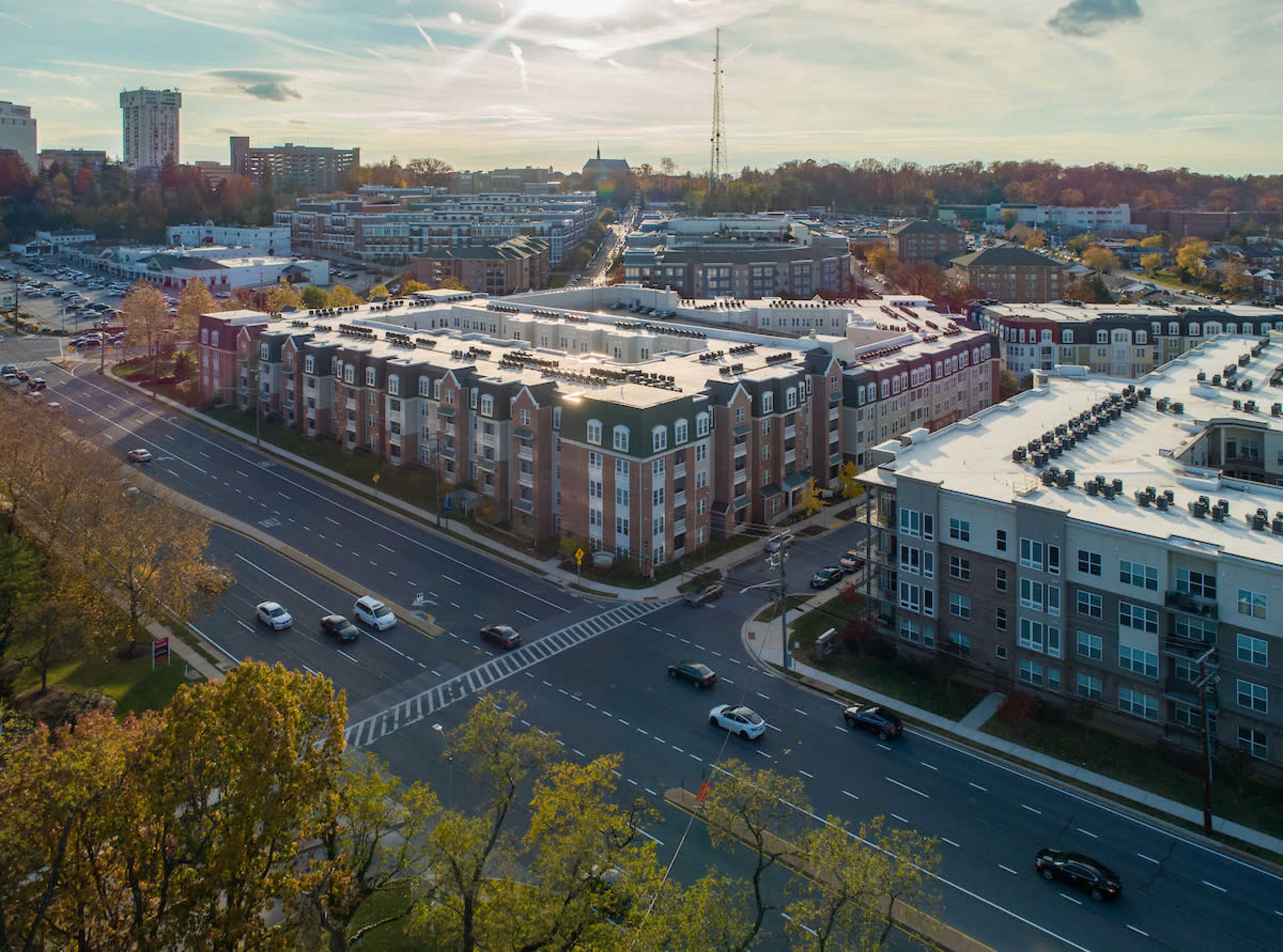 A bustling urban area with several multi-story apartment buildings along a busy street and cars driving in both directions.