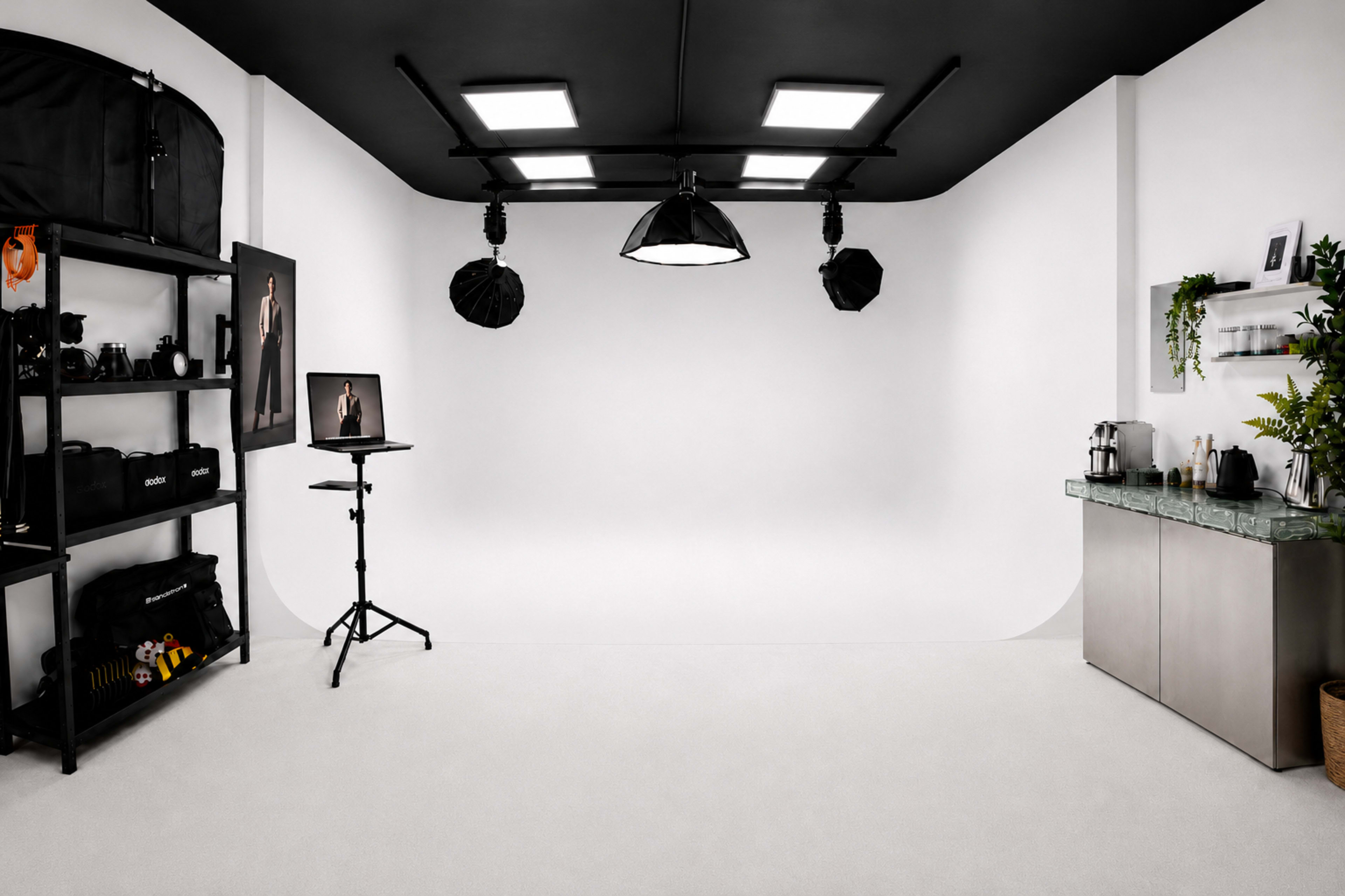 The image shows a well-equipped photography studio with a seamless white backdrop, lighting equipment, and a variety of camera gear stored on shelves.