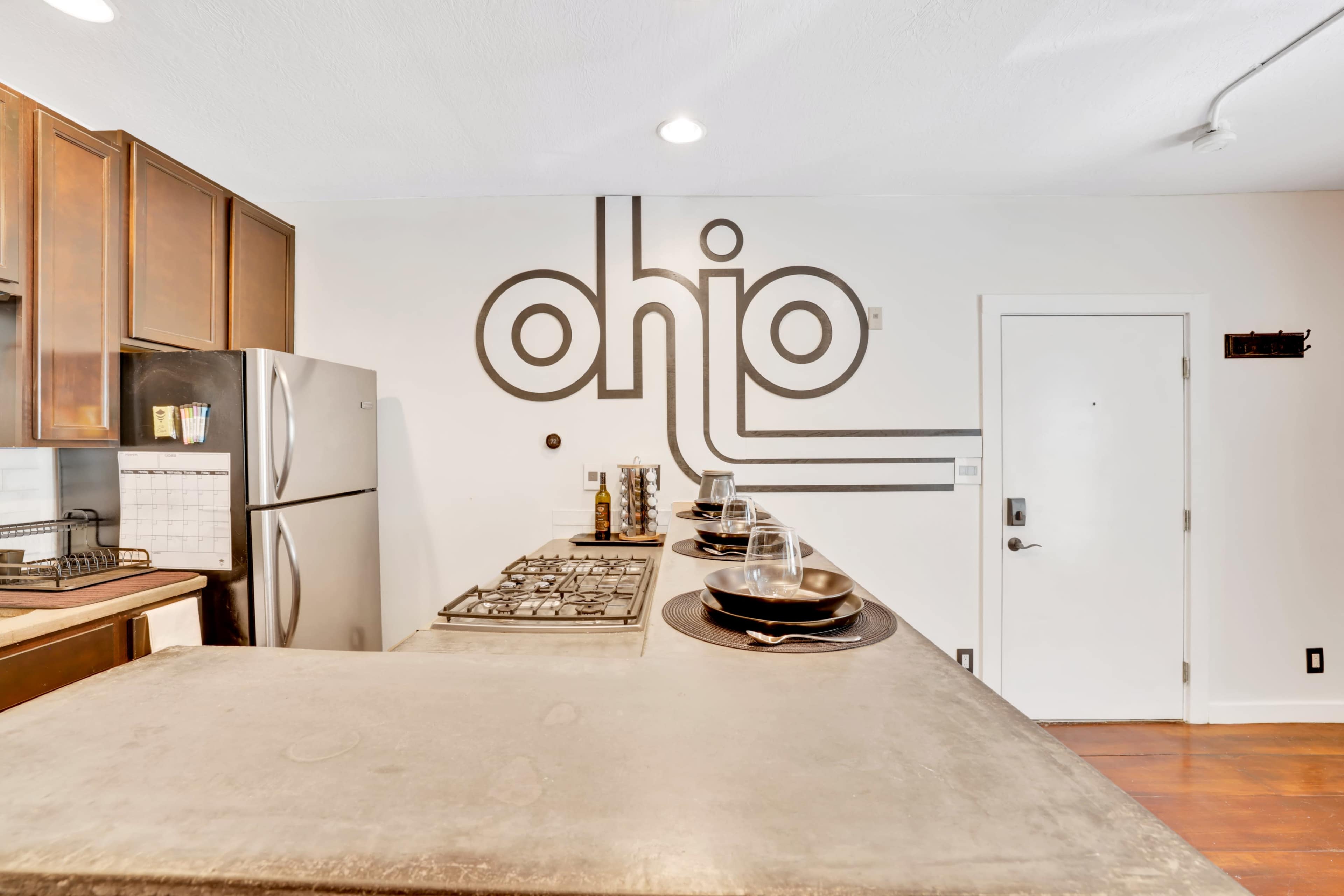 A modern kitchen with a large countertop, stainless steel appliances, and a wall featuring a design that spells "ohio."