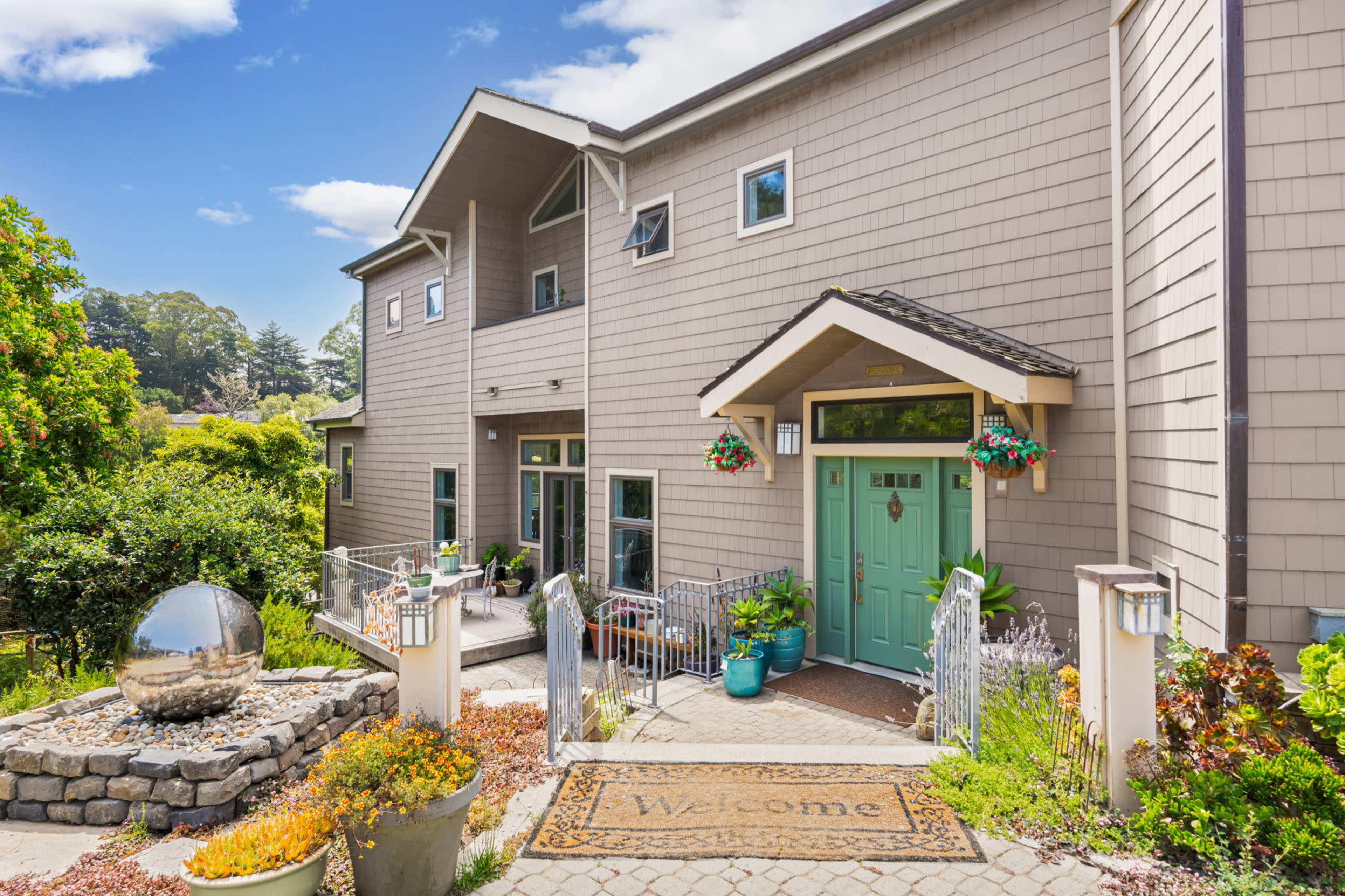A two-story house with a welcoming entrance, featuring double front doors, potted plants, and a decorative stone pathway.