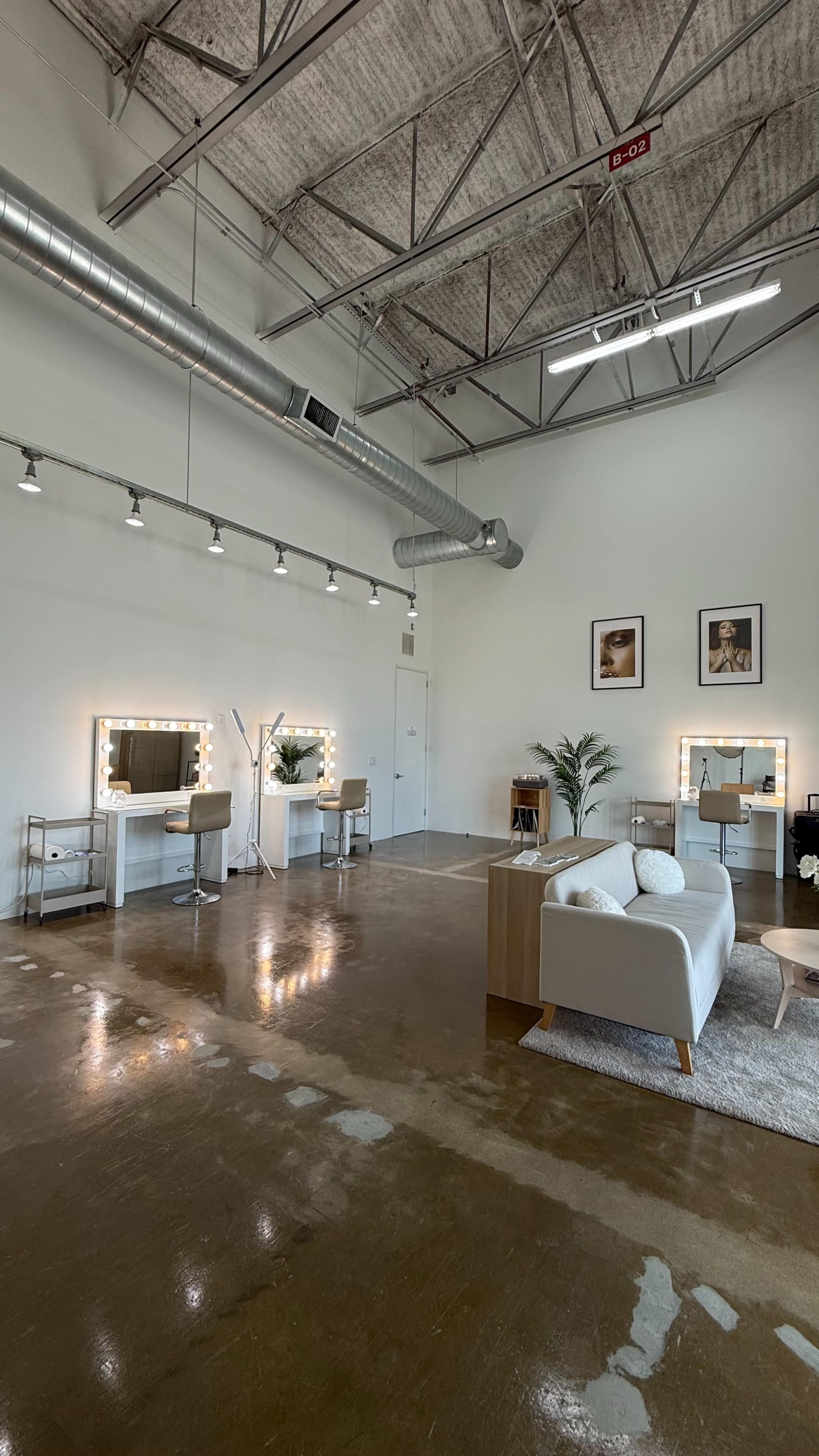 The image shows a spacious, modern interior with two vanity stations, a seating area, and framed artwork on the walls.