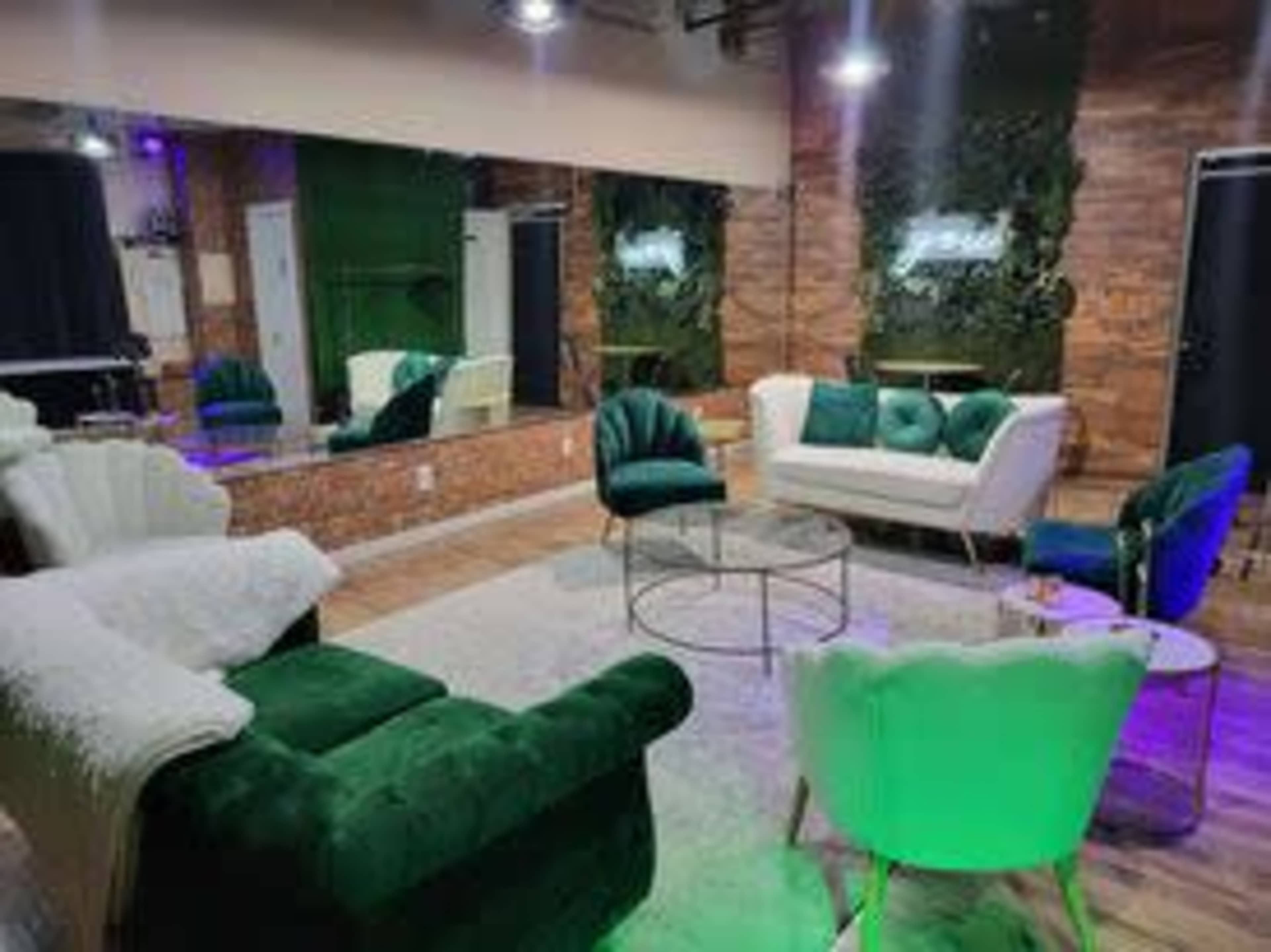 A modern lounge area with green and white seating, a glass coffee table, and a mirrored wall, surrounded by wooden accents and plants.