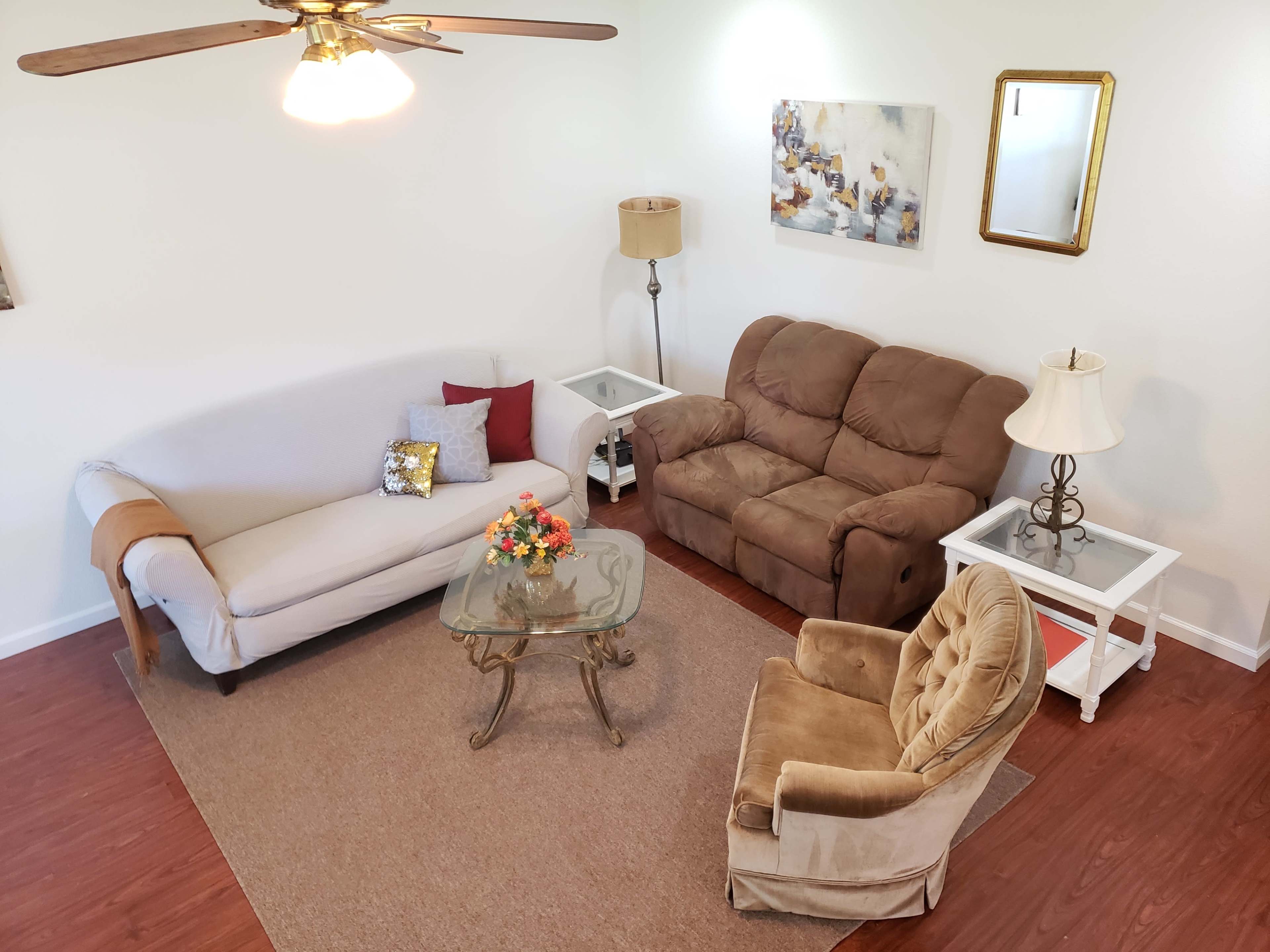 A living room with a light-colored sofa, a brown loveseat, a glass coffee table, and a beige rug.