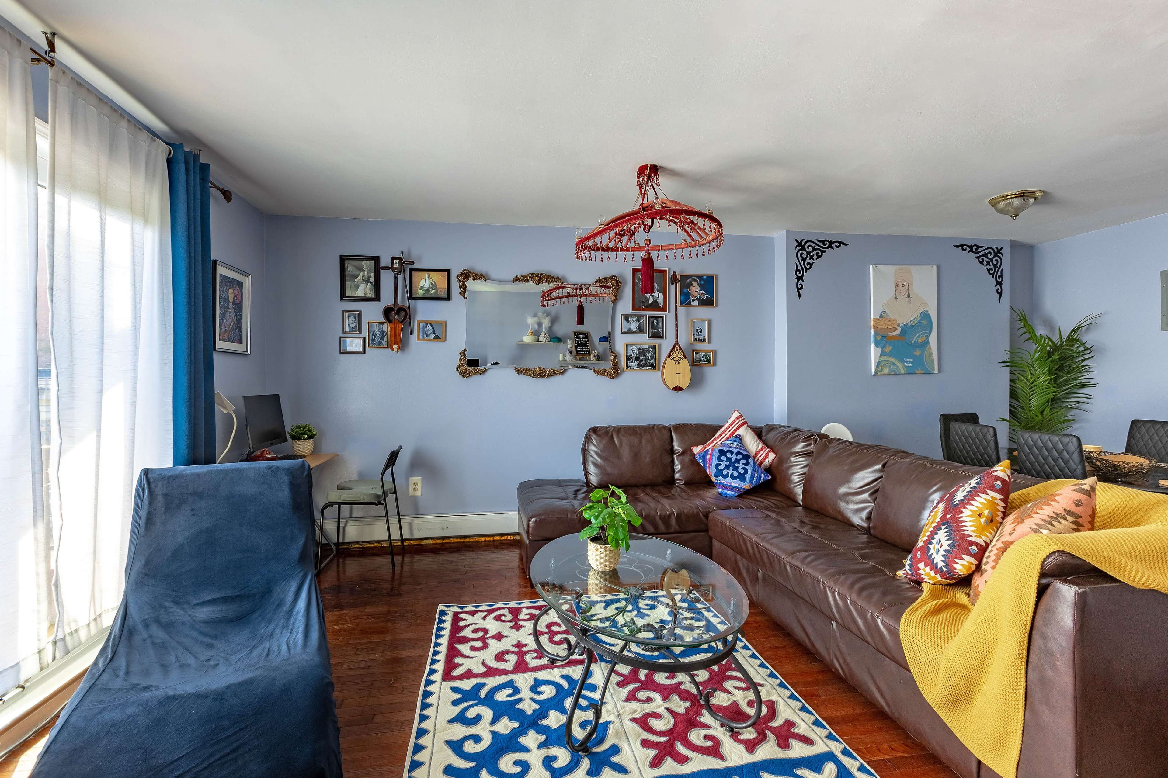 A living room features a brown leather sofa, a glass coffee table, and colorful decorative elements on the walls.