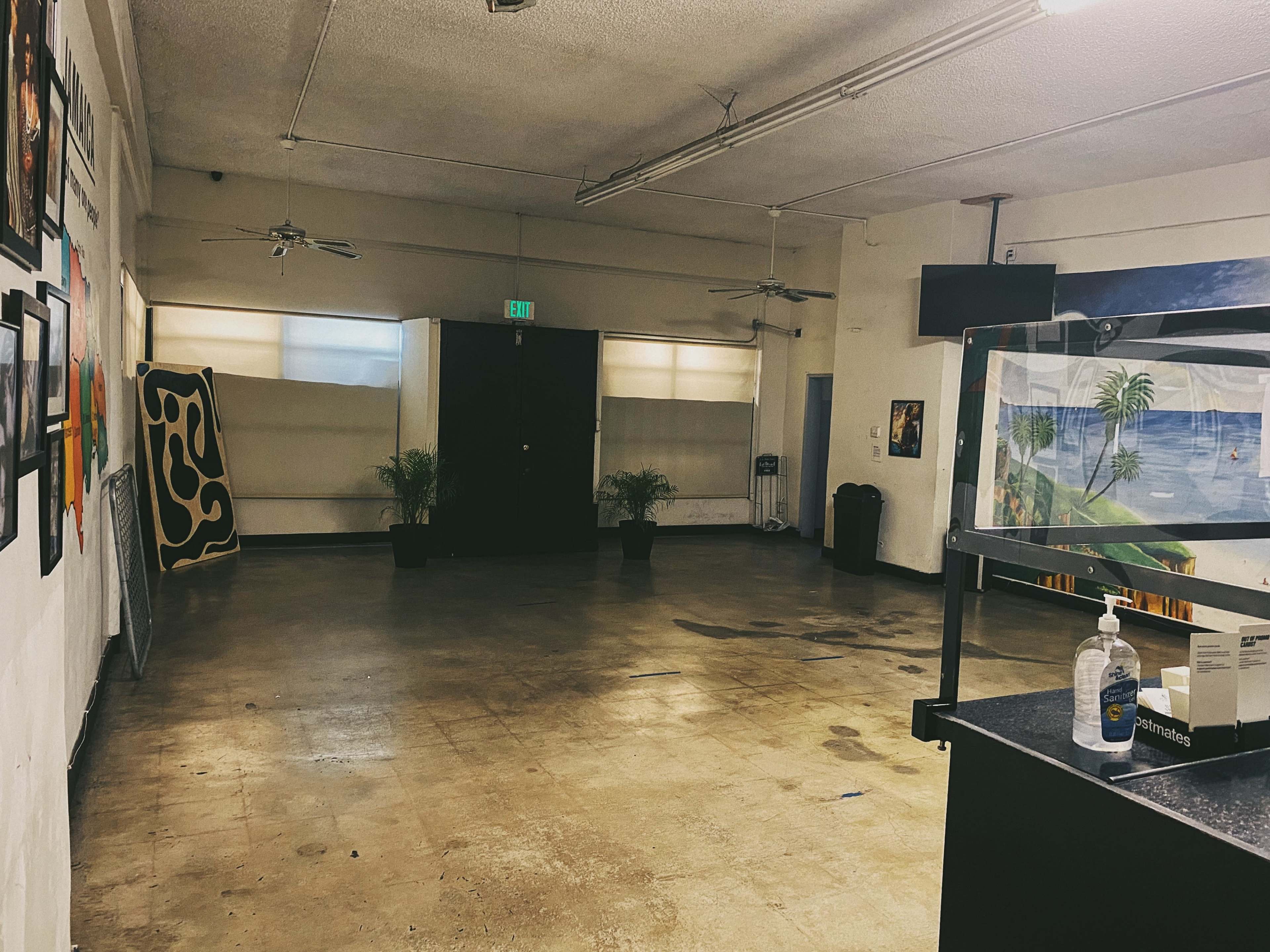 An empty room with a concrete floor, two plants in pots, and artwork displayed on the walls.