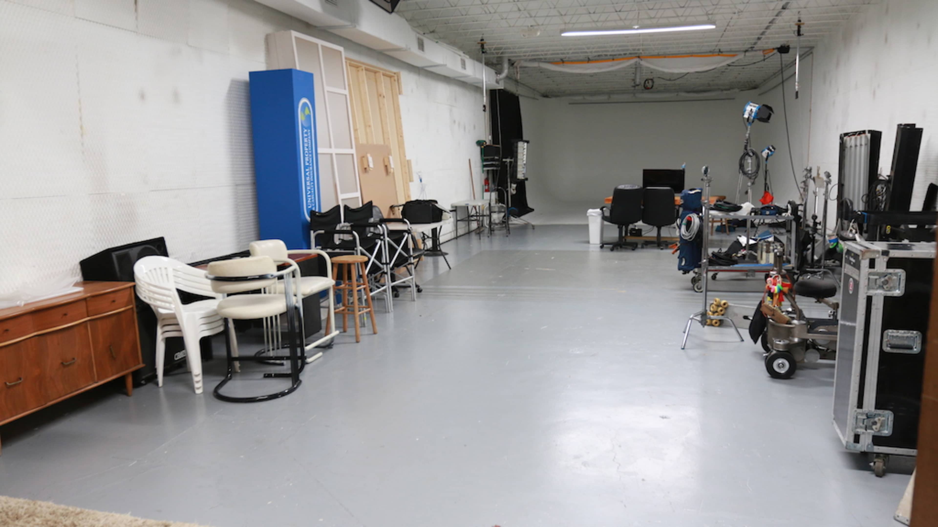 The image shows a spacious studio with various pieces of equipment, empty chairs, and a plain backdrop.