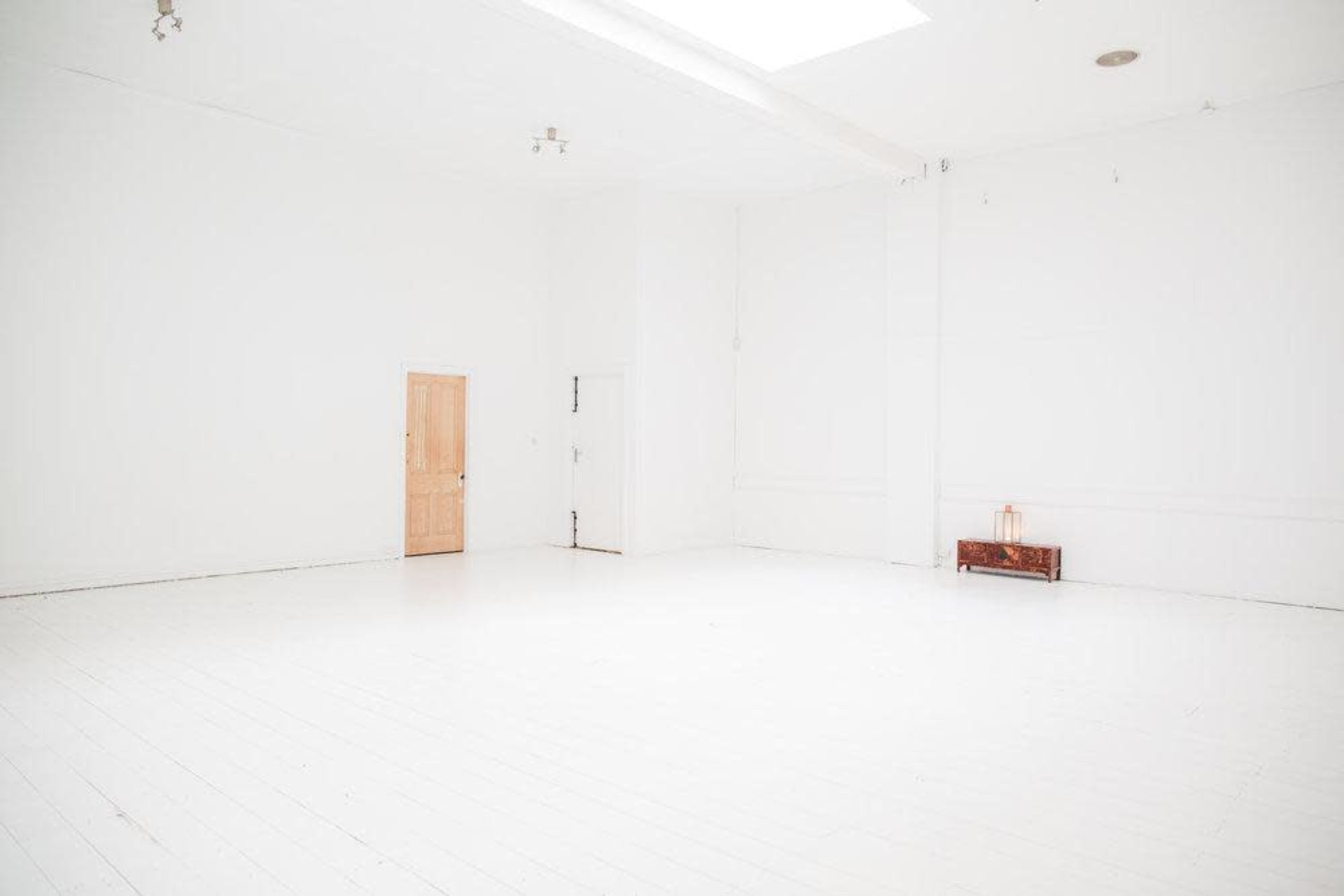 The image shows a spacious, empty white room with two doors and a small wooden bench against the wall.