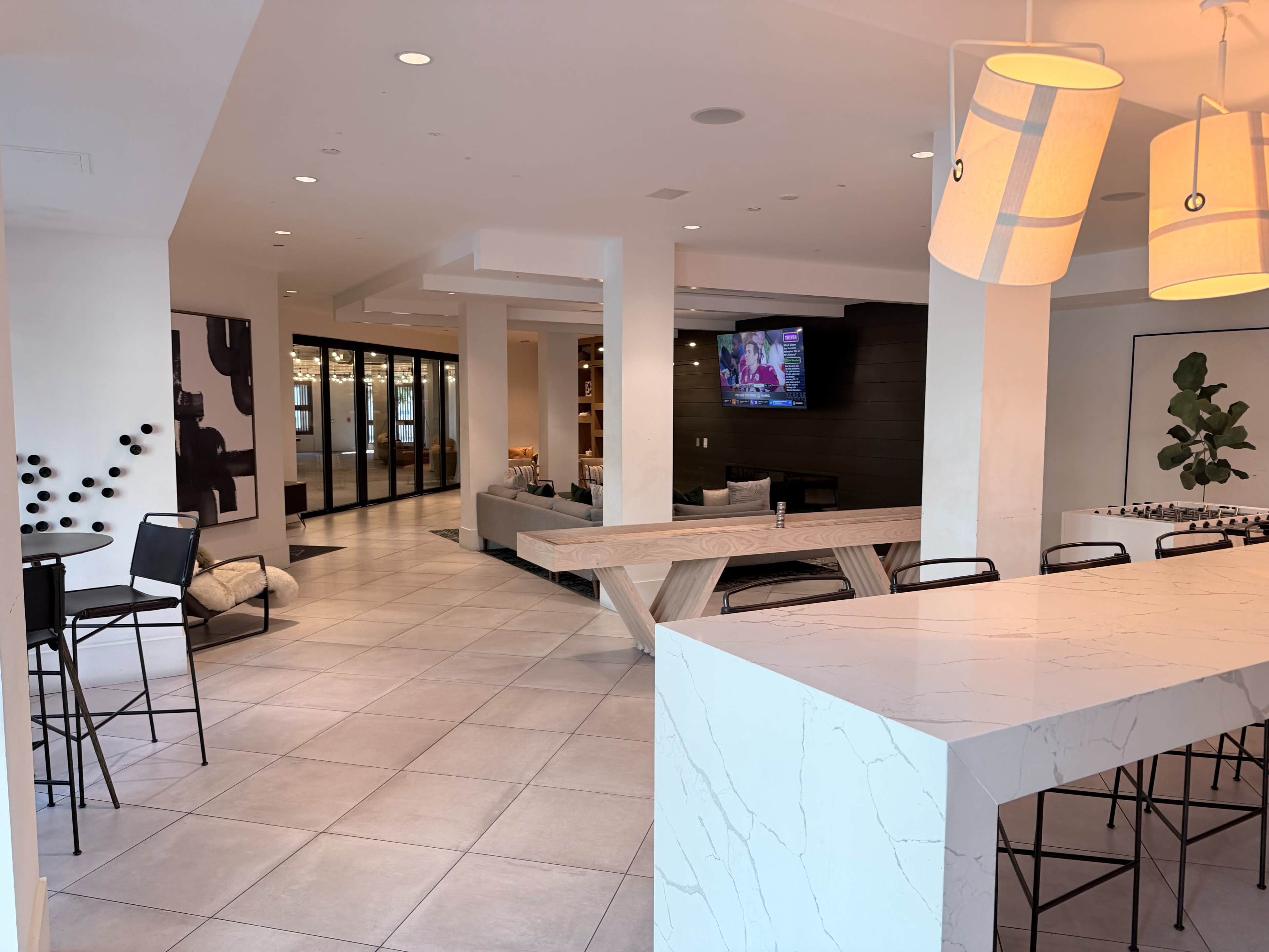 The image shows a modern open-concept lobby area featuring a large marble counter, a wooden communal table, and stylish seating arrangements.