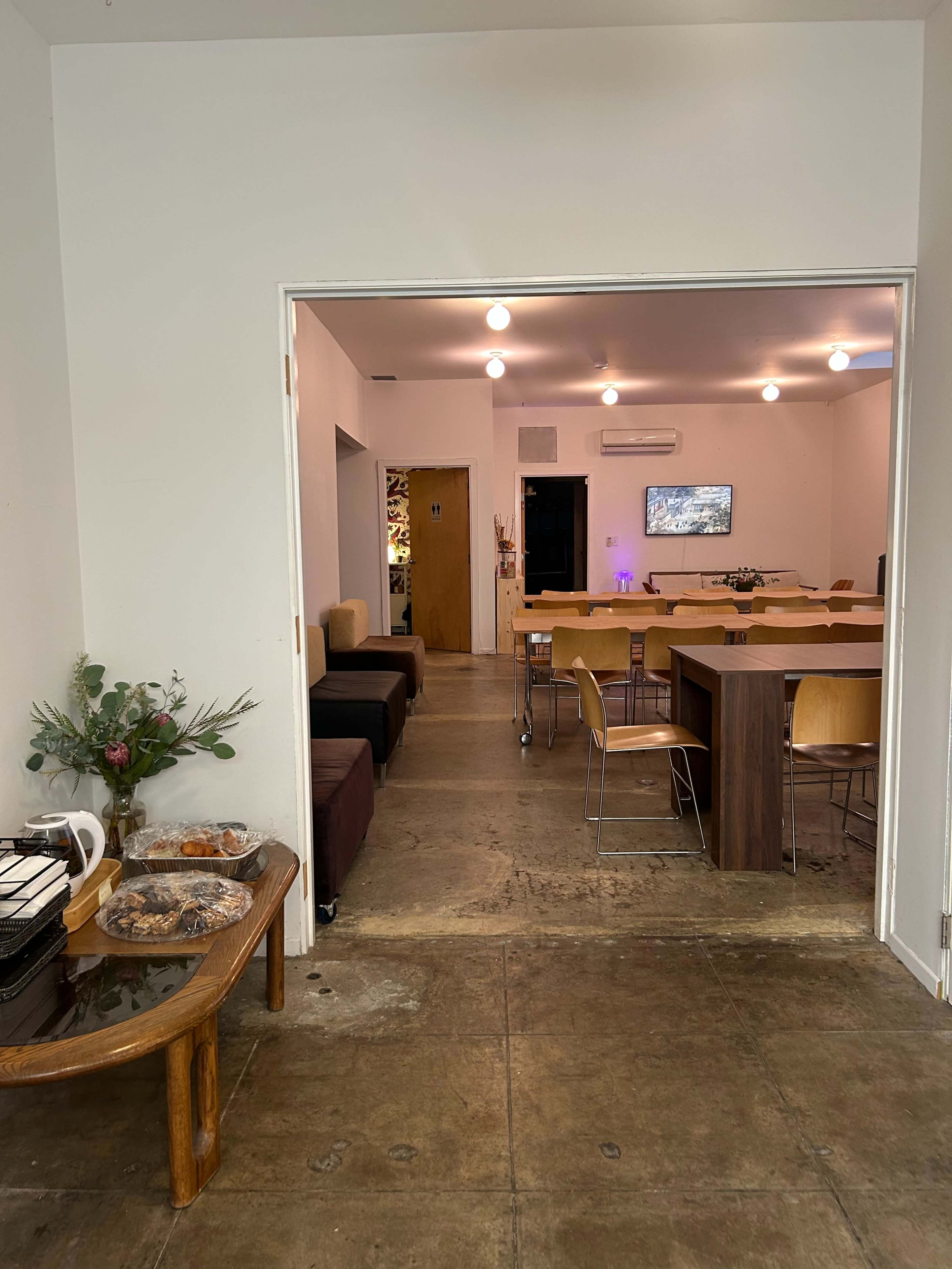 A brightly lit communal space features dining tables, chairs, and a television in the background.