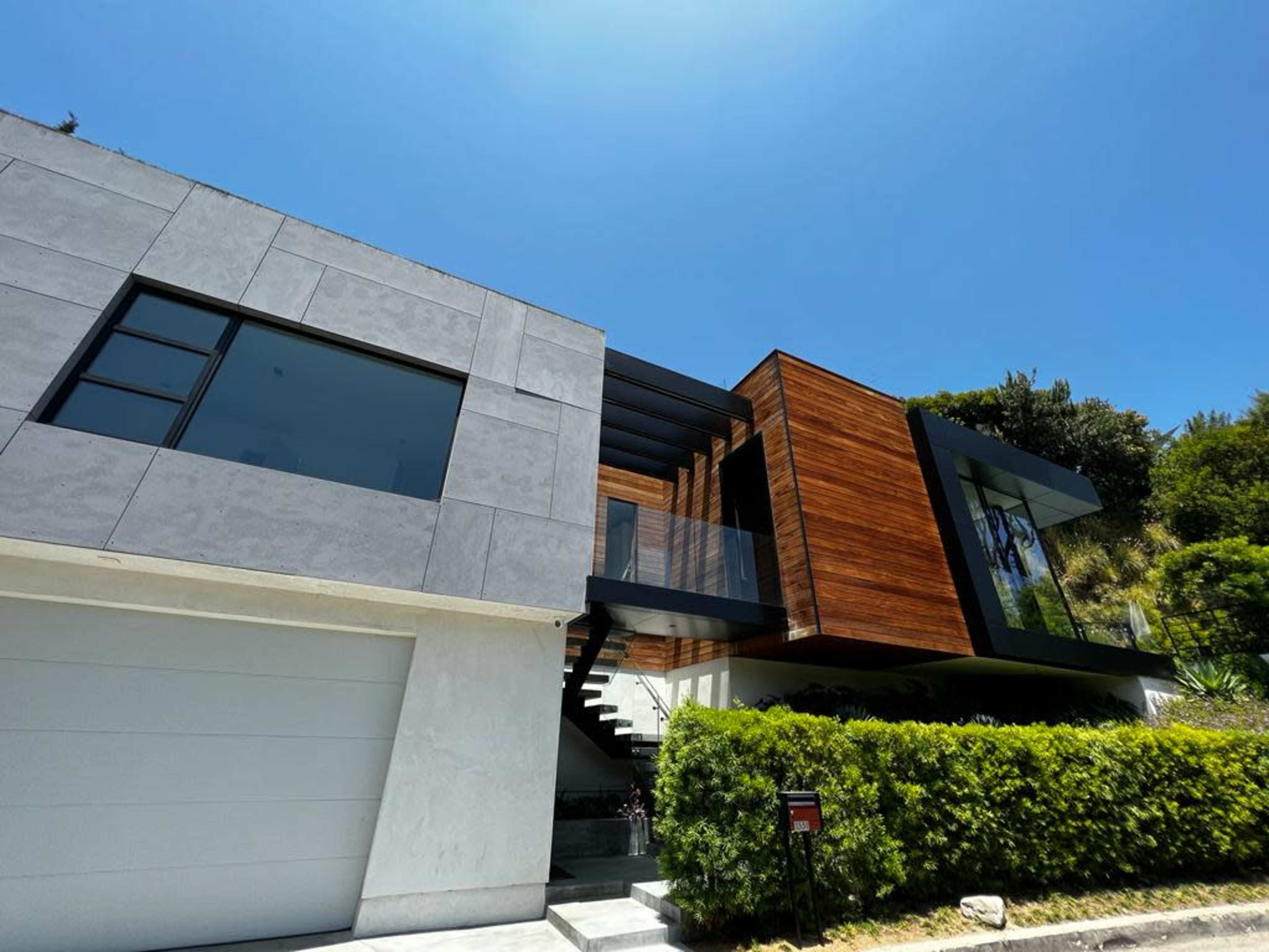 A modern house features a combination of gray and wooden facades, with a staircase leading up to the entrance.