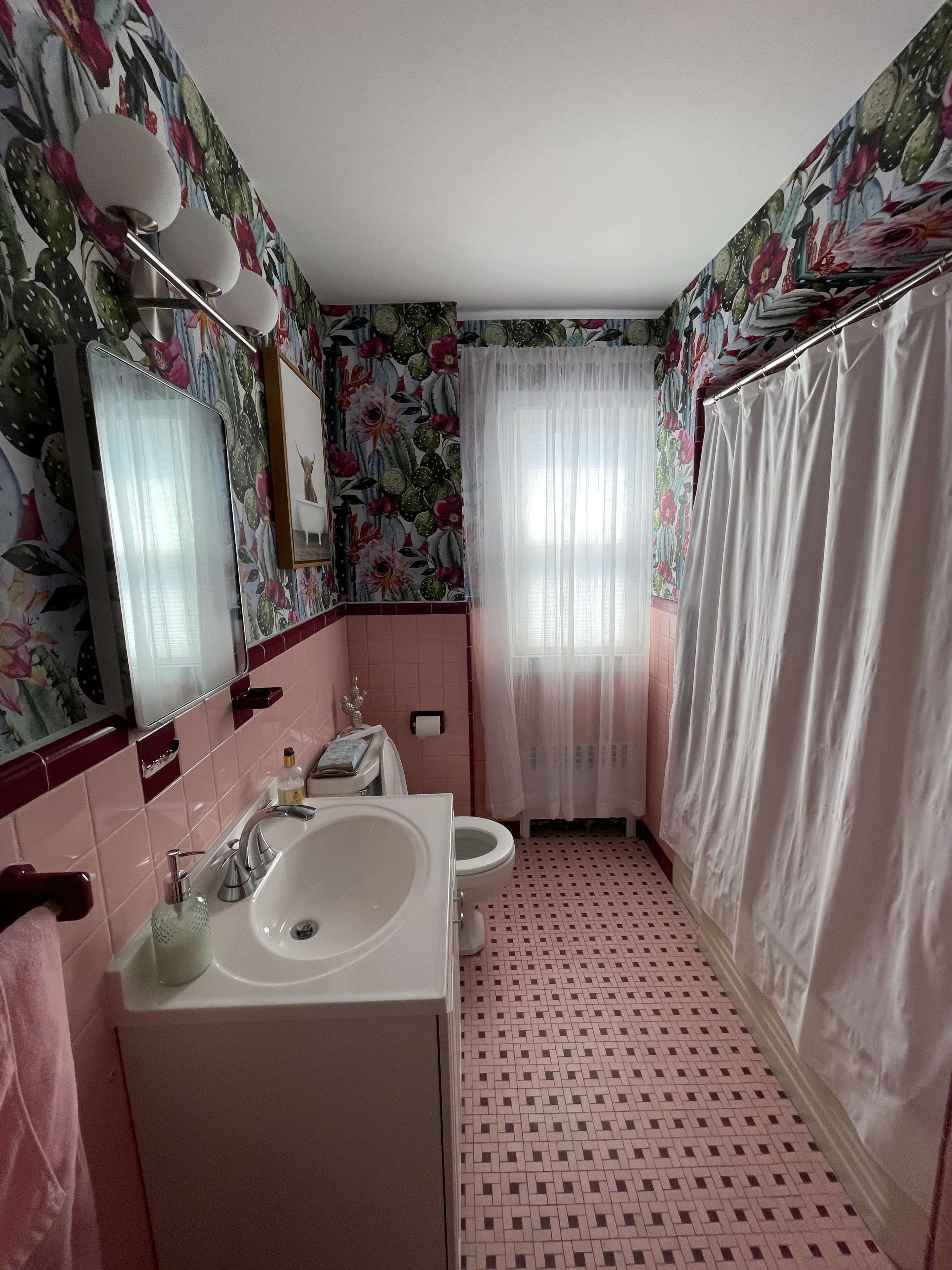 The bathroom features pink tiles, a shower curtain, a sink with a mirror, and floral wallpaper.