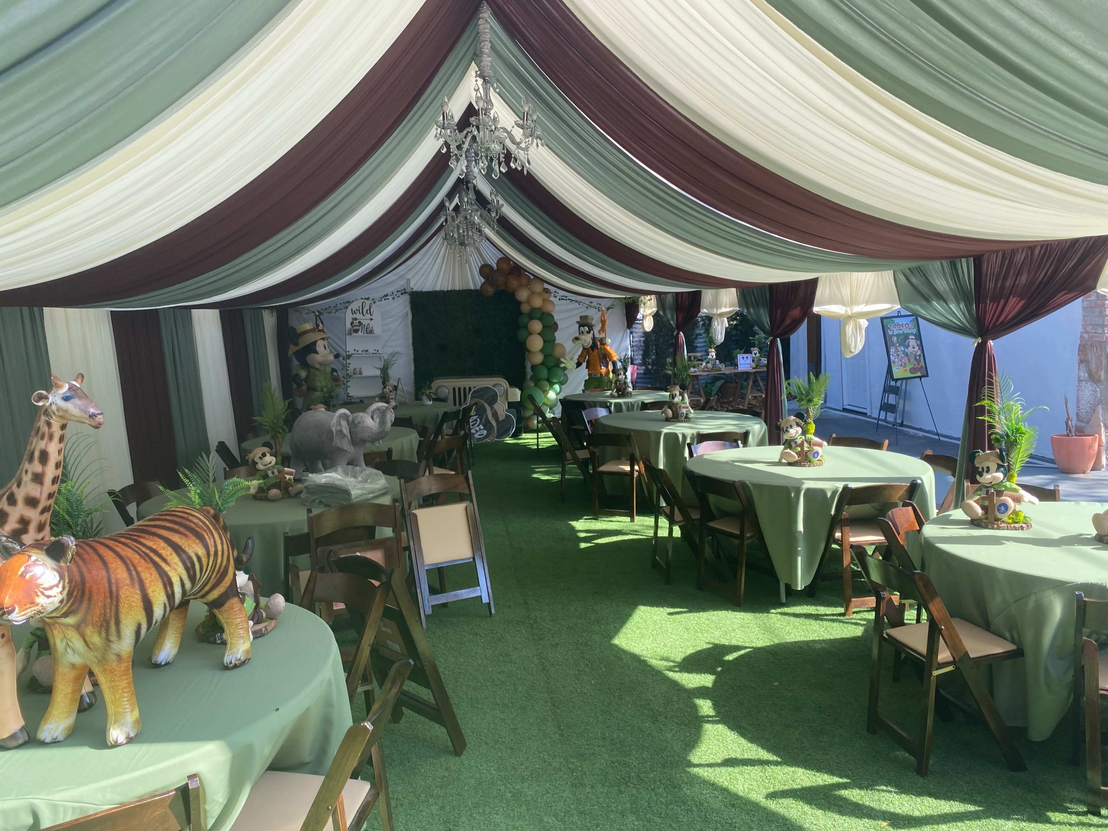 The scene features a decorated tent with green carpet, tables covered in light green tablecloths, and animal figurines, including a tiger, giraffe, and elephant, arranged throughout.