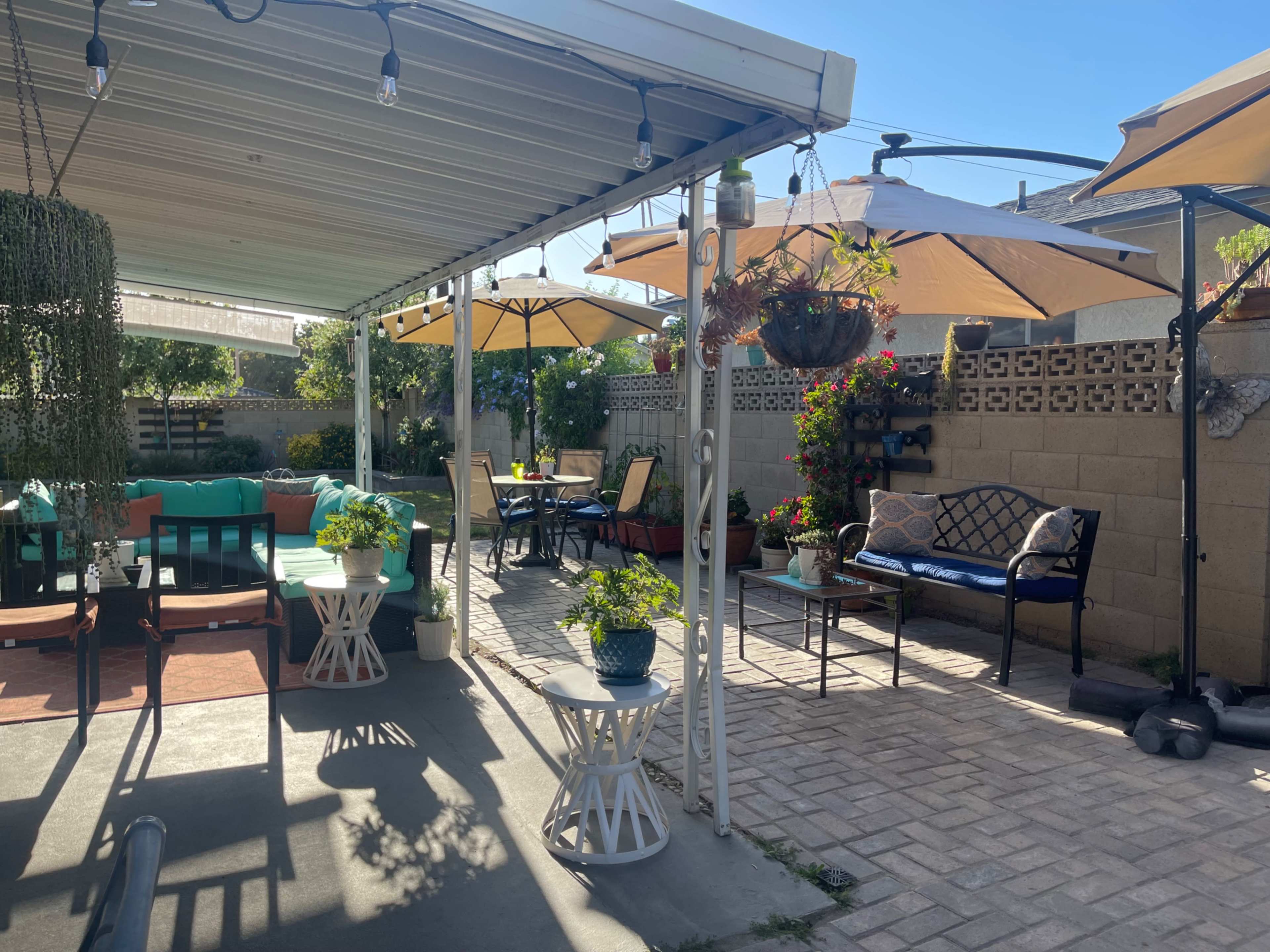 A patio area with various seating arrangements, umbrellas, and potted plants under a shaded roof.