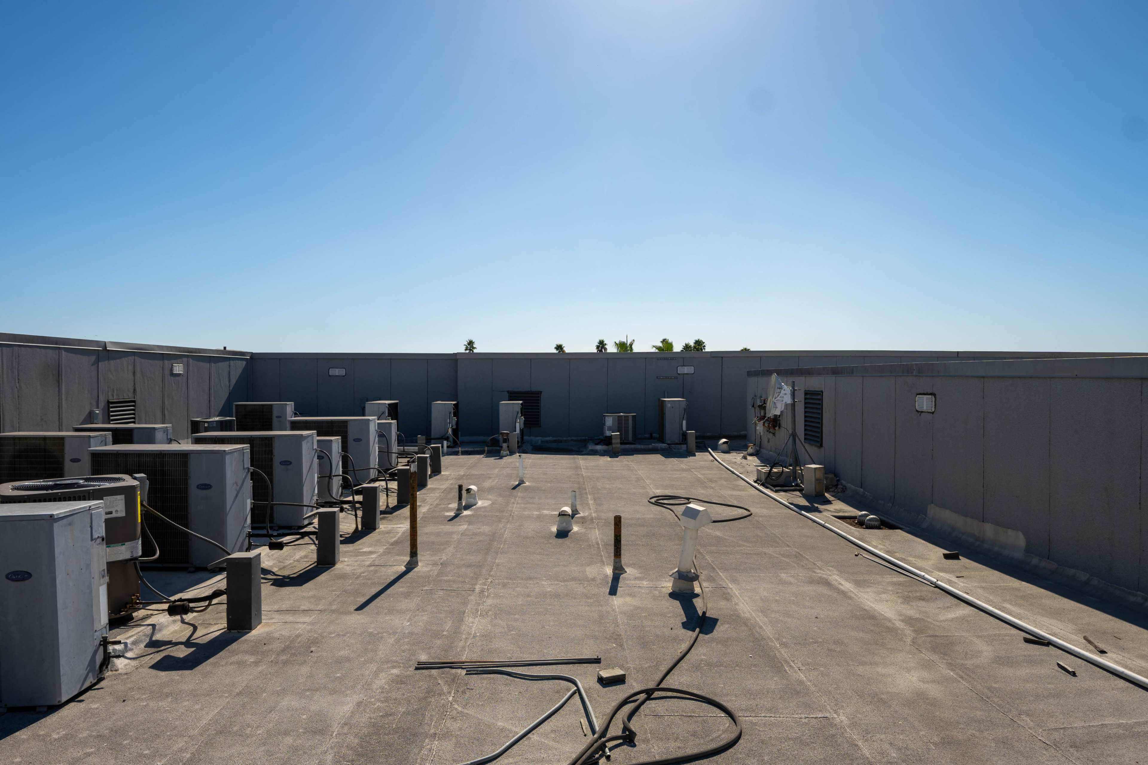 A flat rooftop equipped with multiple air conditioning units and various vent pipes under a clear blue sky.