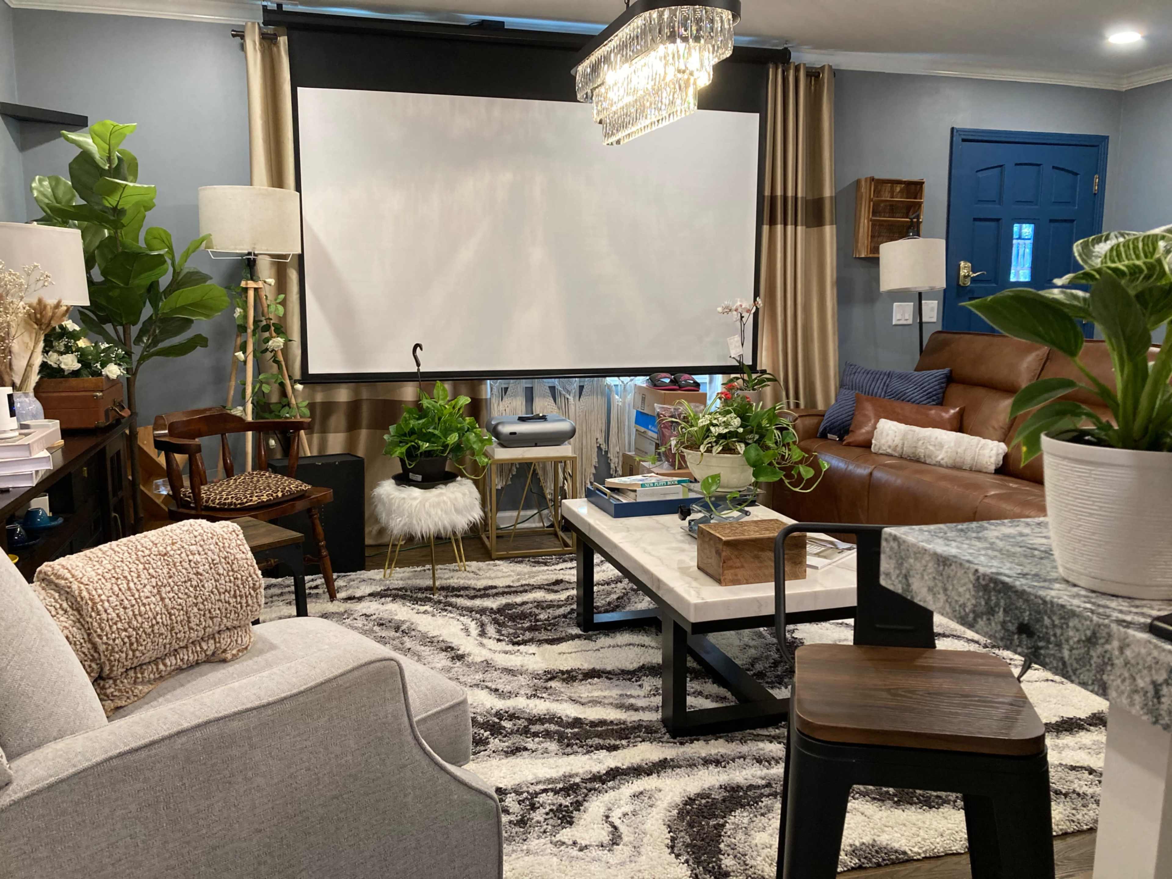 A cozy living room features a large projection screen, comfortable seating, decorative plants, and a patterned area rug.