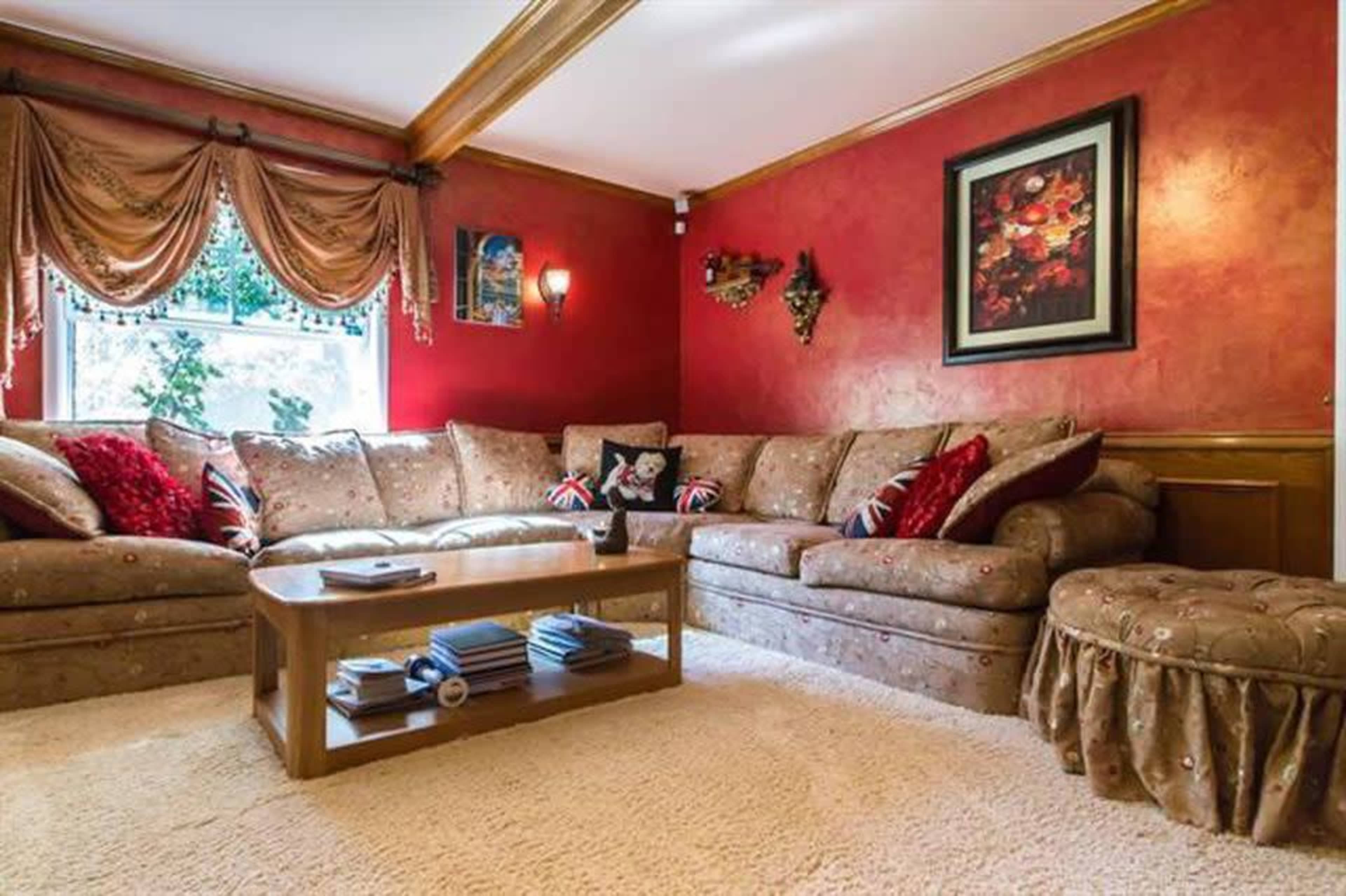 A spacious living room features a large, L-shaped beige couch with decorative pillows, a wooden coffee table, and a plush carpet under soft lighting.