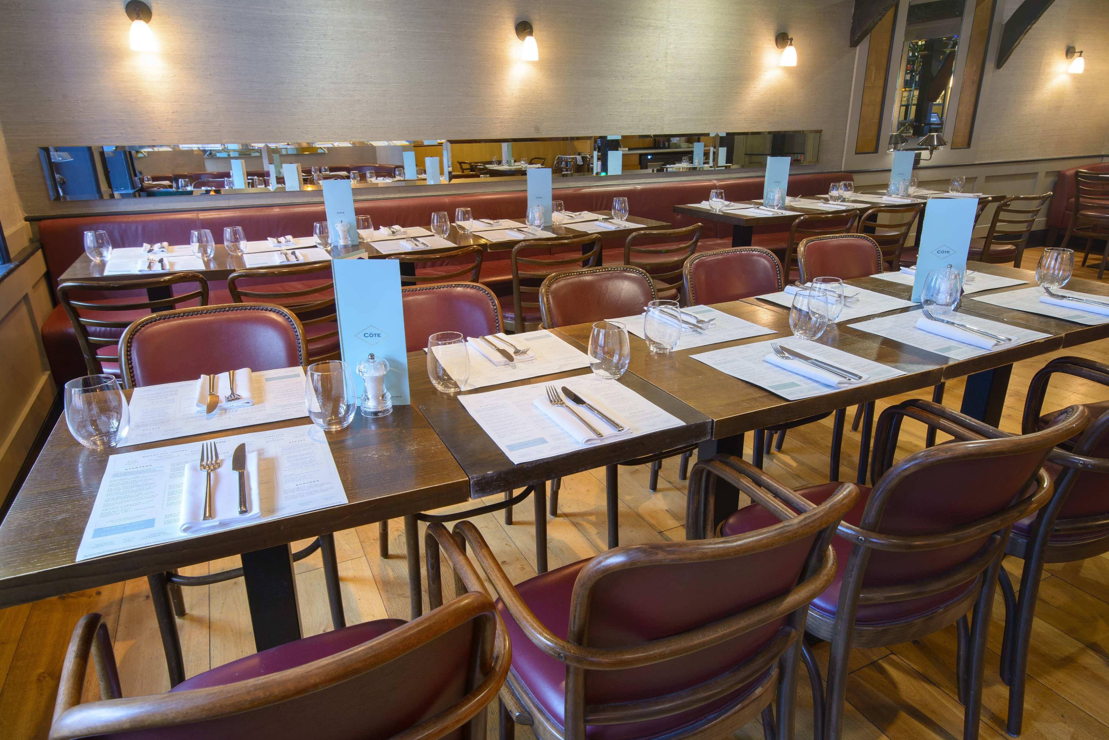 The image shows a restaurant interior with neatly arranged tables set with menus, cutlery, and glassware.
