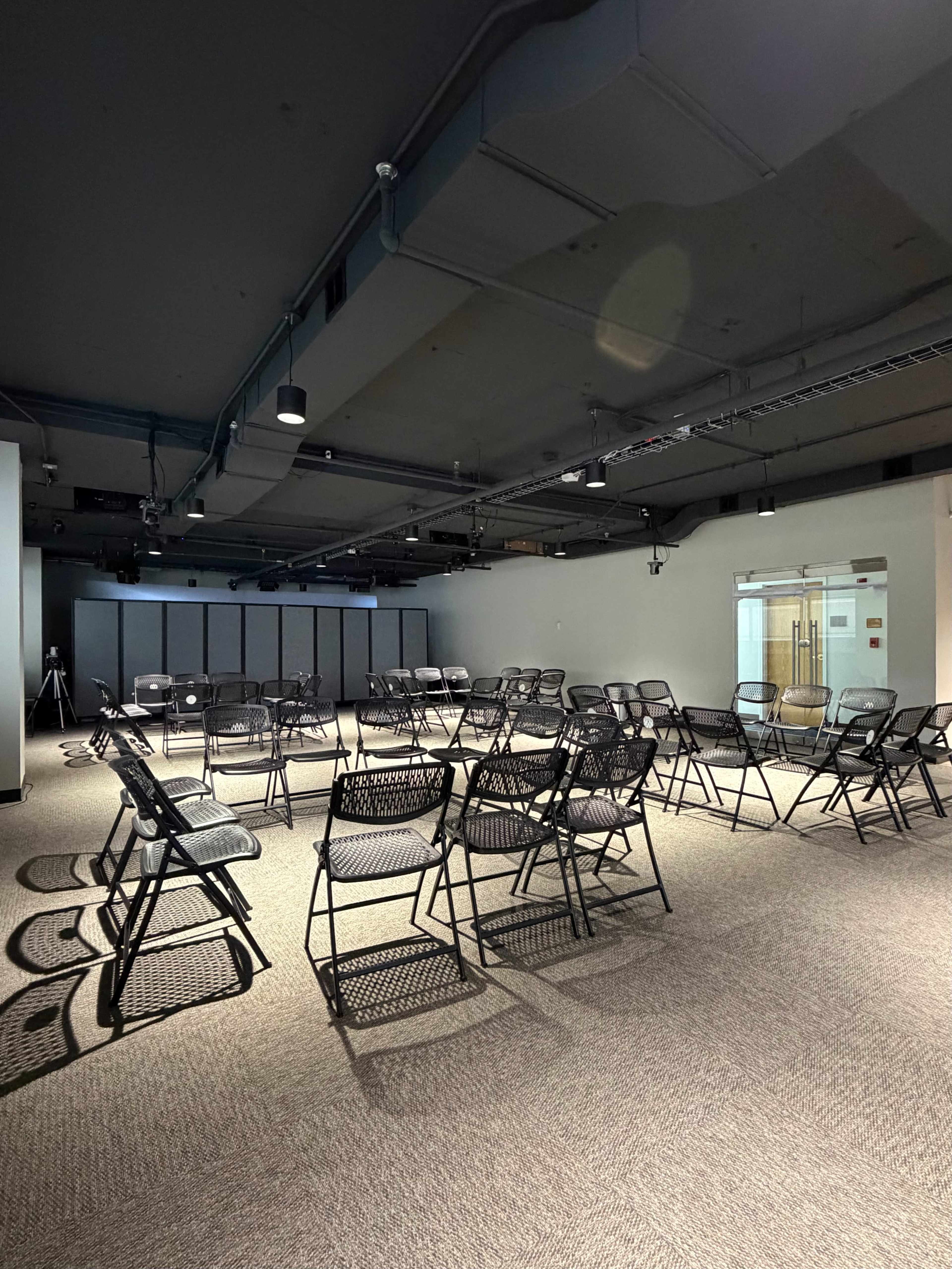 The image shows a large room set up with black folding chairs arranged in a circular pattern on a carpeted floor.