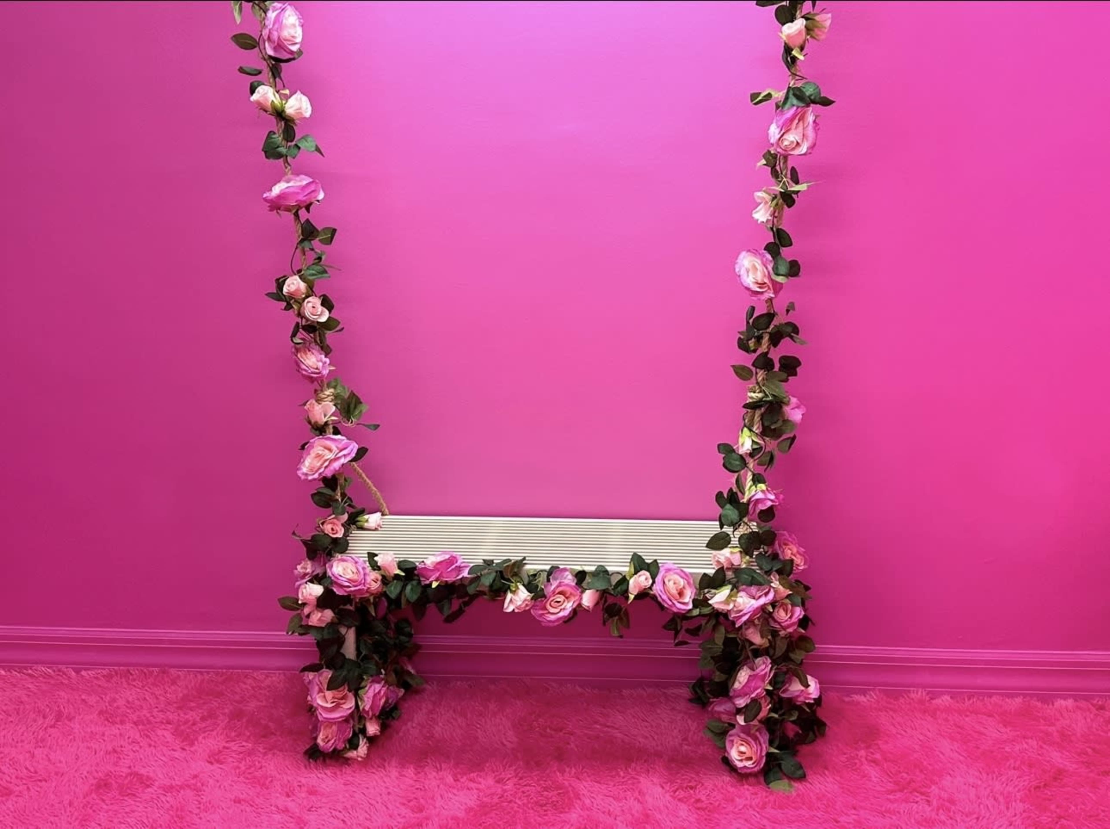 A pink wall is adorned with a floral arrangement of roses and greenery around a decorative bench.