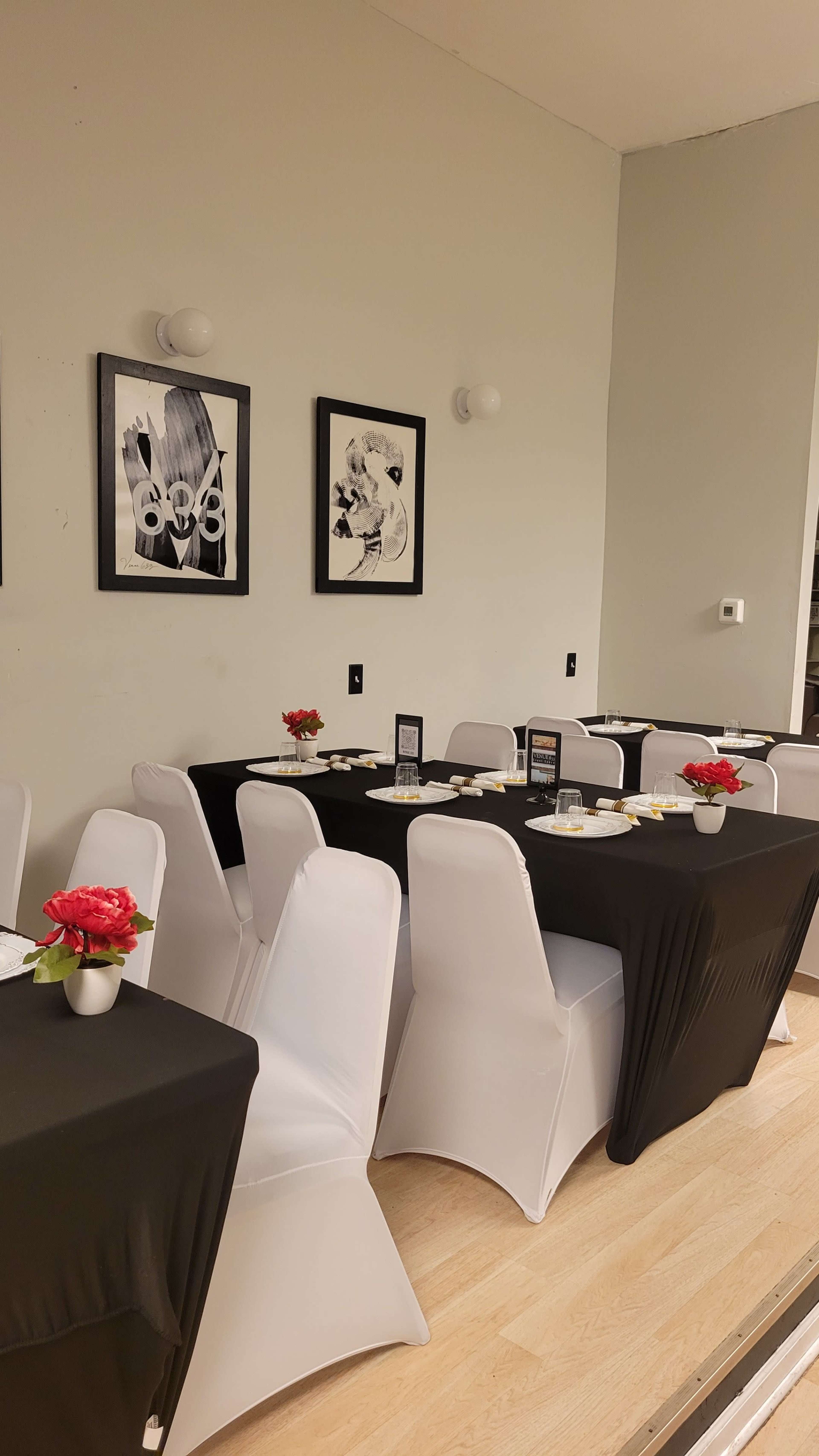 A dining area features several tables covered with black and white tablecloths, adorned with small floral centerpieces, and framed artwork on the walls.