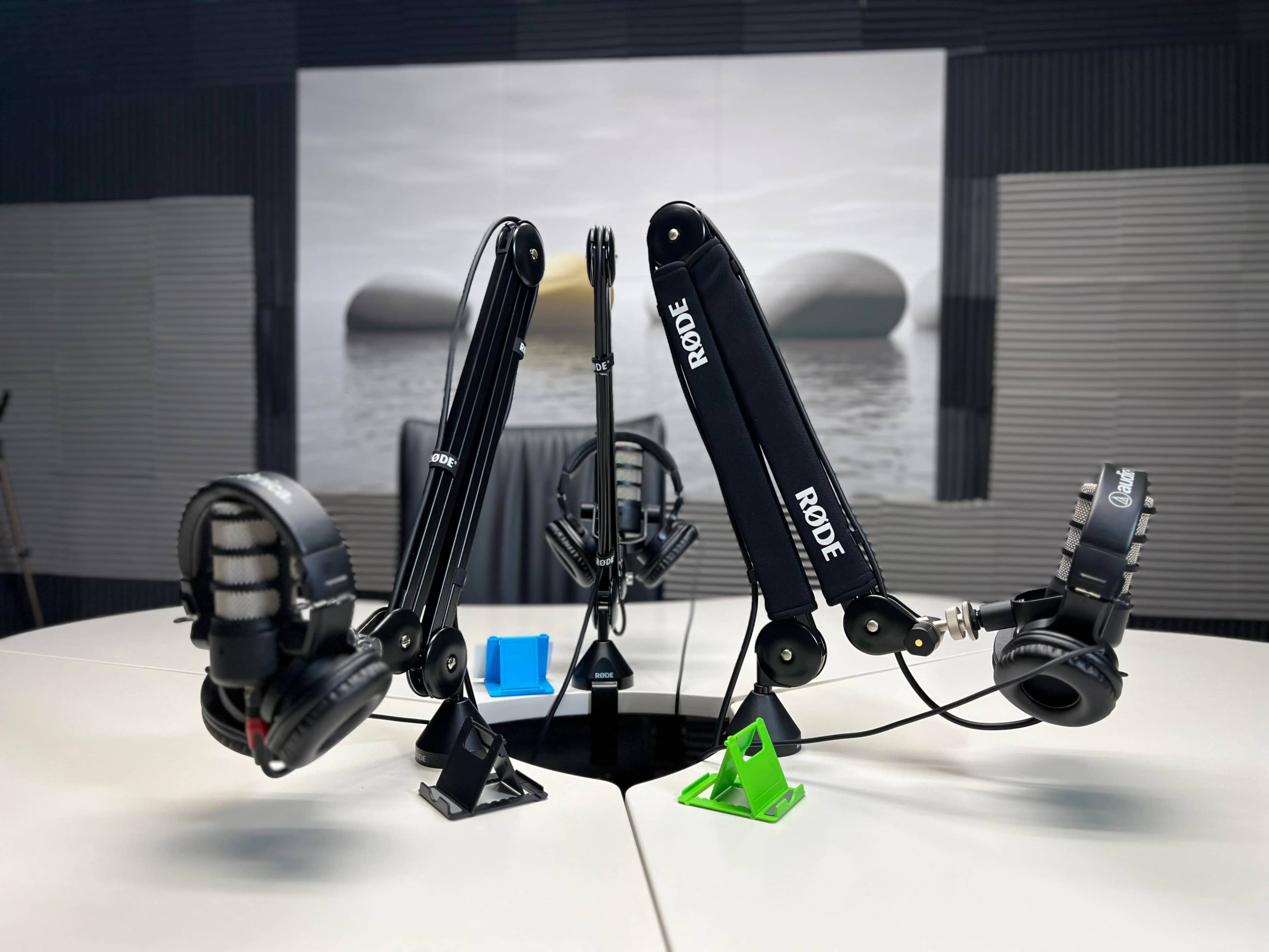 A podcasting setup with two adjustable microphone stands, headphones, and a central microphone on a round table.