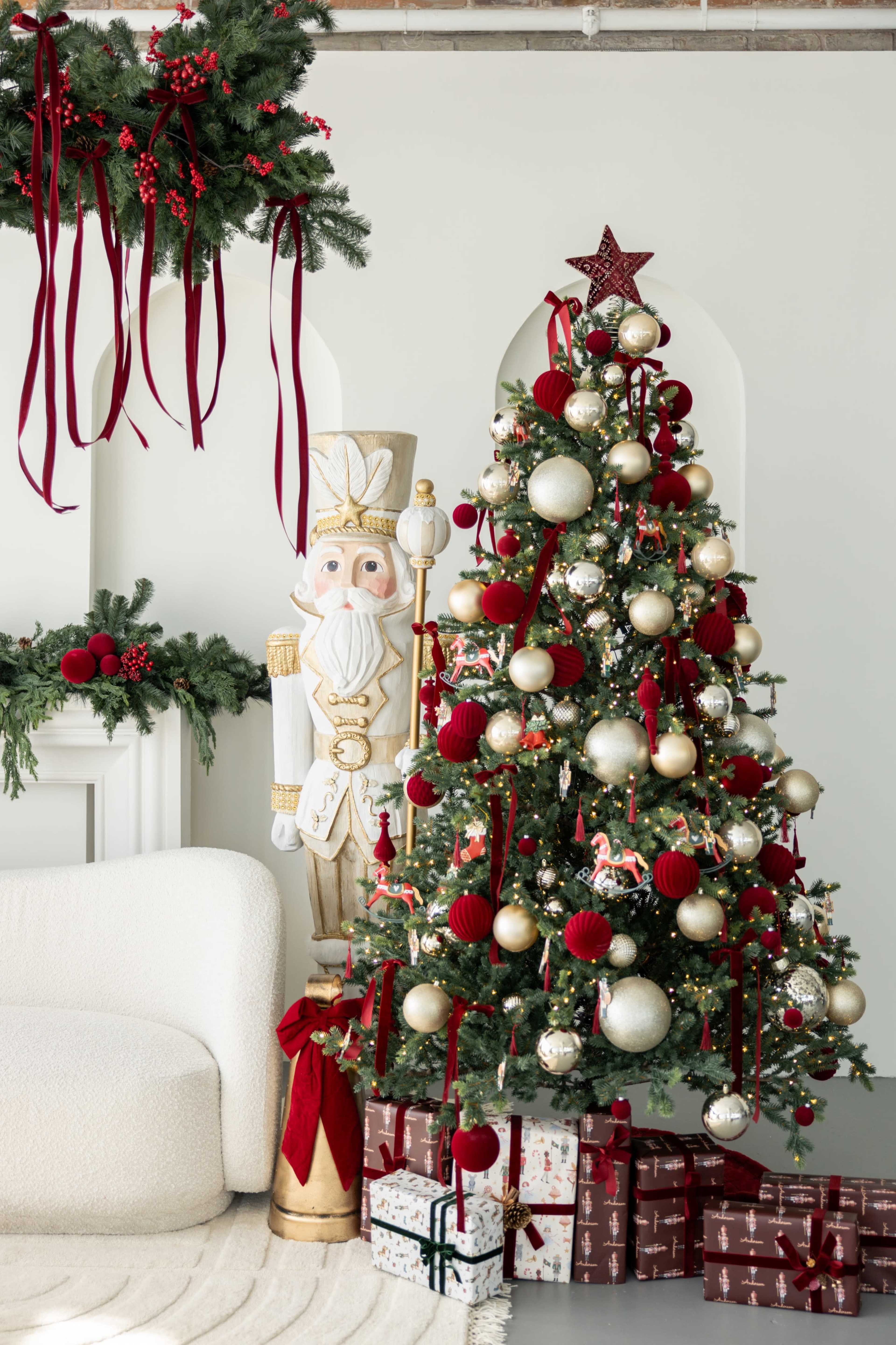 The image features a decorated Christmas tree adorned with red and gold ornaments, alongside a large nutcracker figure, with wrapped gifts positioned at its base.