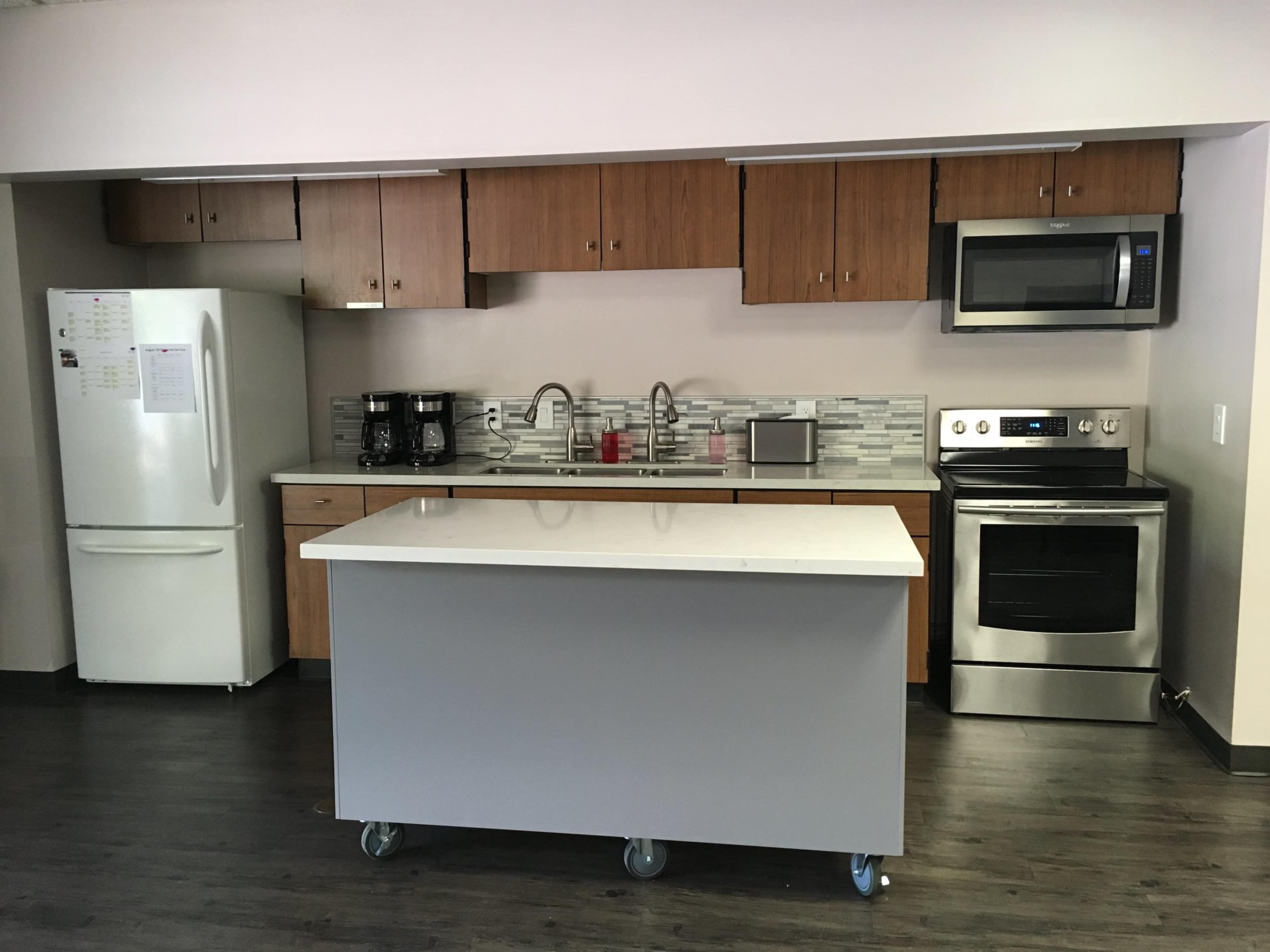 A modern kitchen with wooden cabinets, stainless steel appliances, a white countertop island on wheels, and a tiled backsplash.