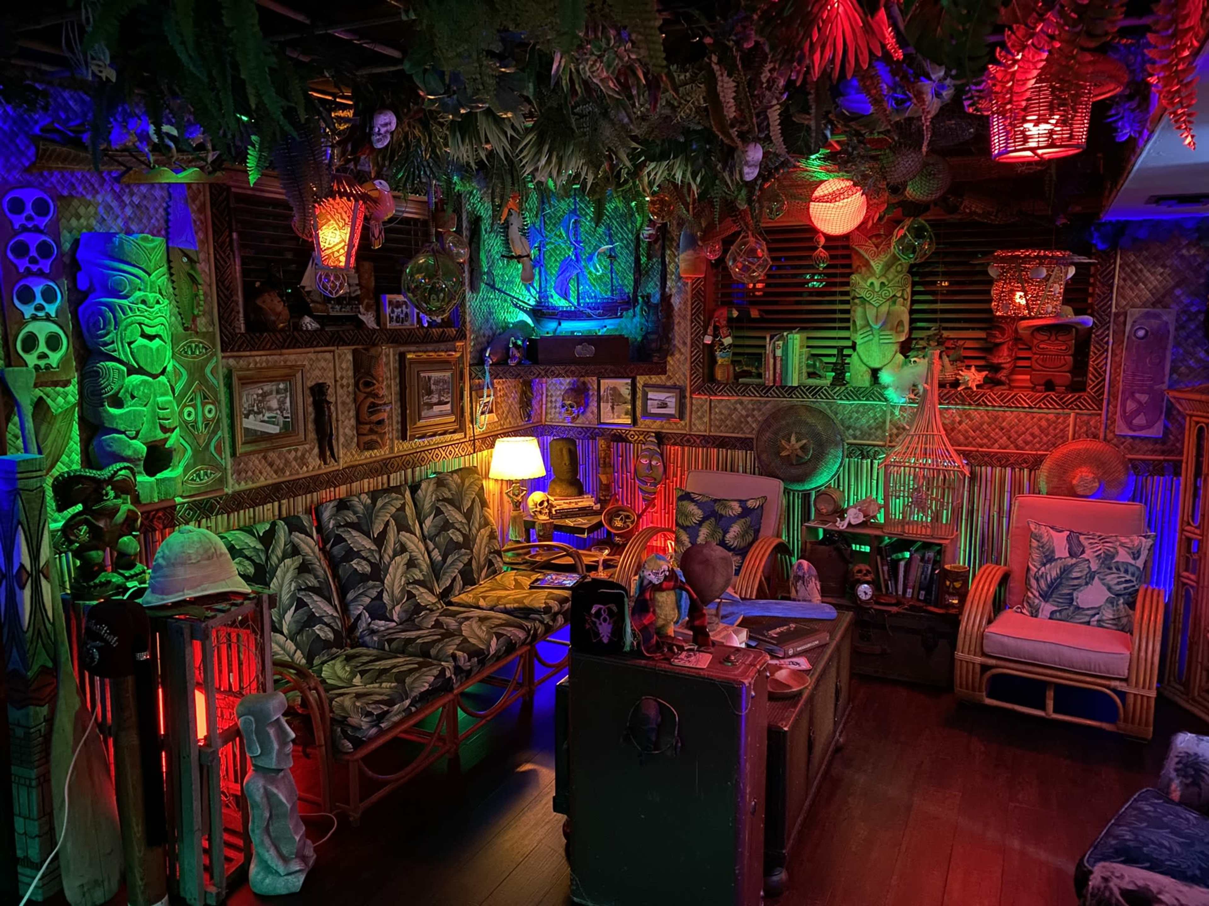 A cozy room decorated in a tropical theme with colorful lighting, tiki masks, and lush greenery.