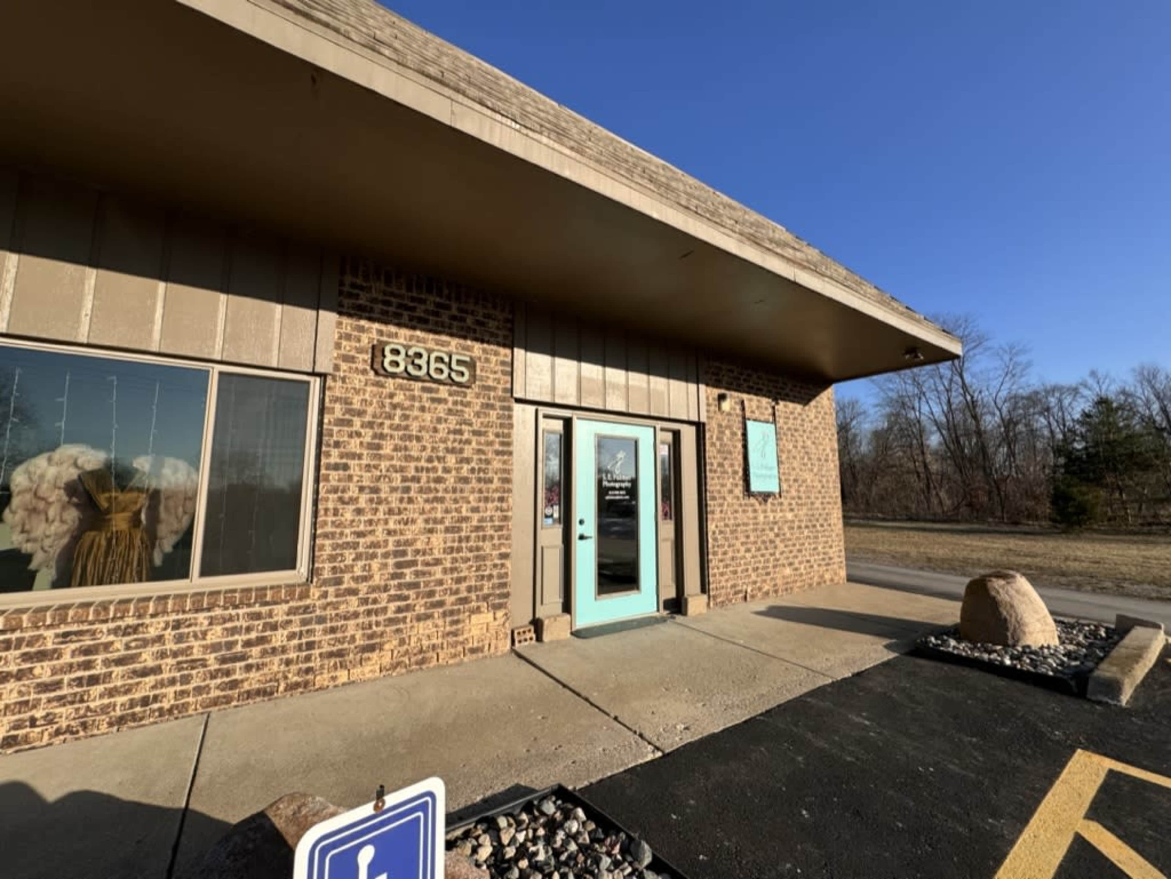 The image shows a brick building with a turquoise door, marked with the number 8365, and features a sign in front indicating accessible parking.
