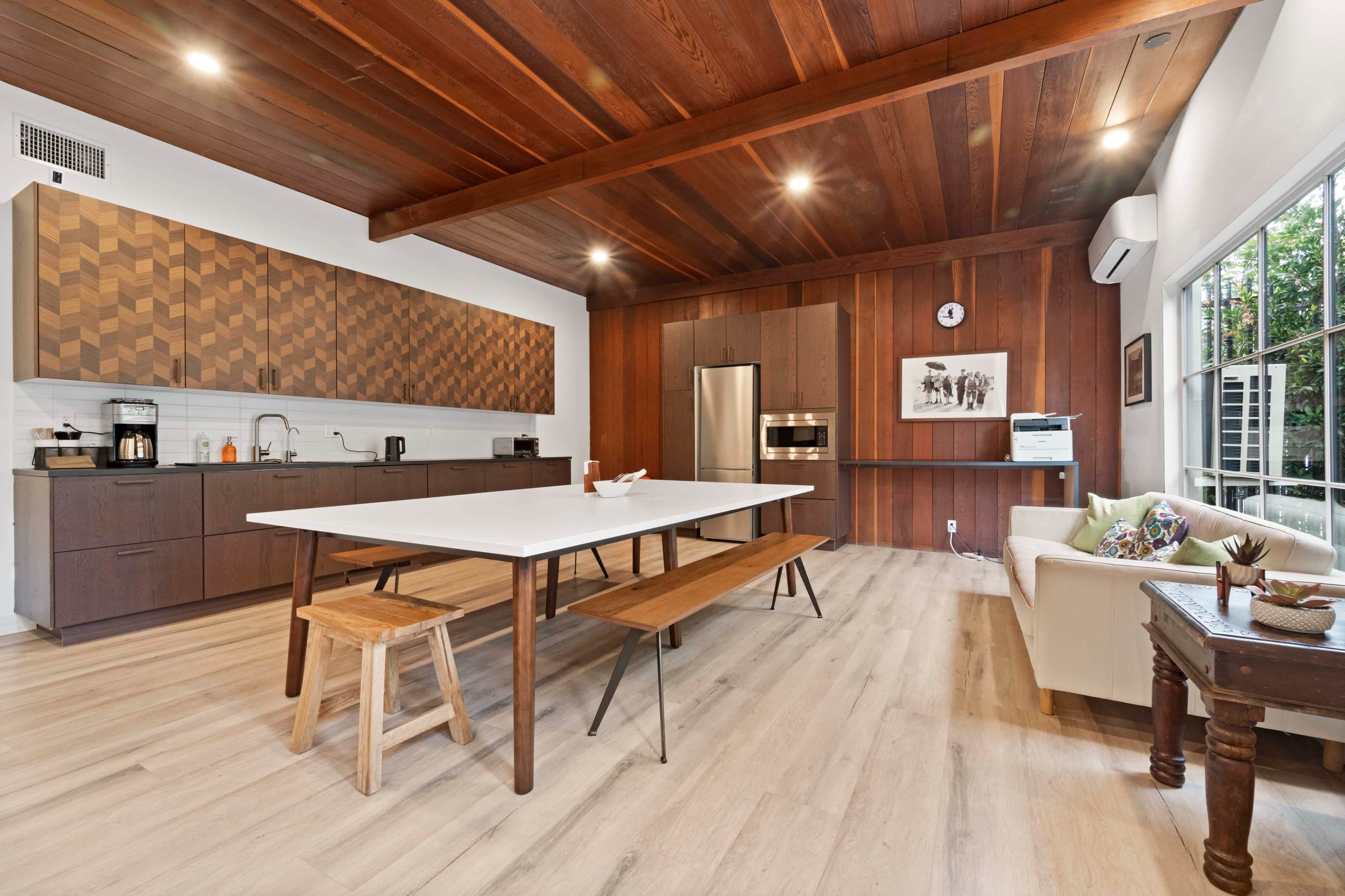 A modern kitchen with a large wooden table and benches, featuring a patterned cabinetry wall and stainless steel appliances.