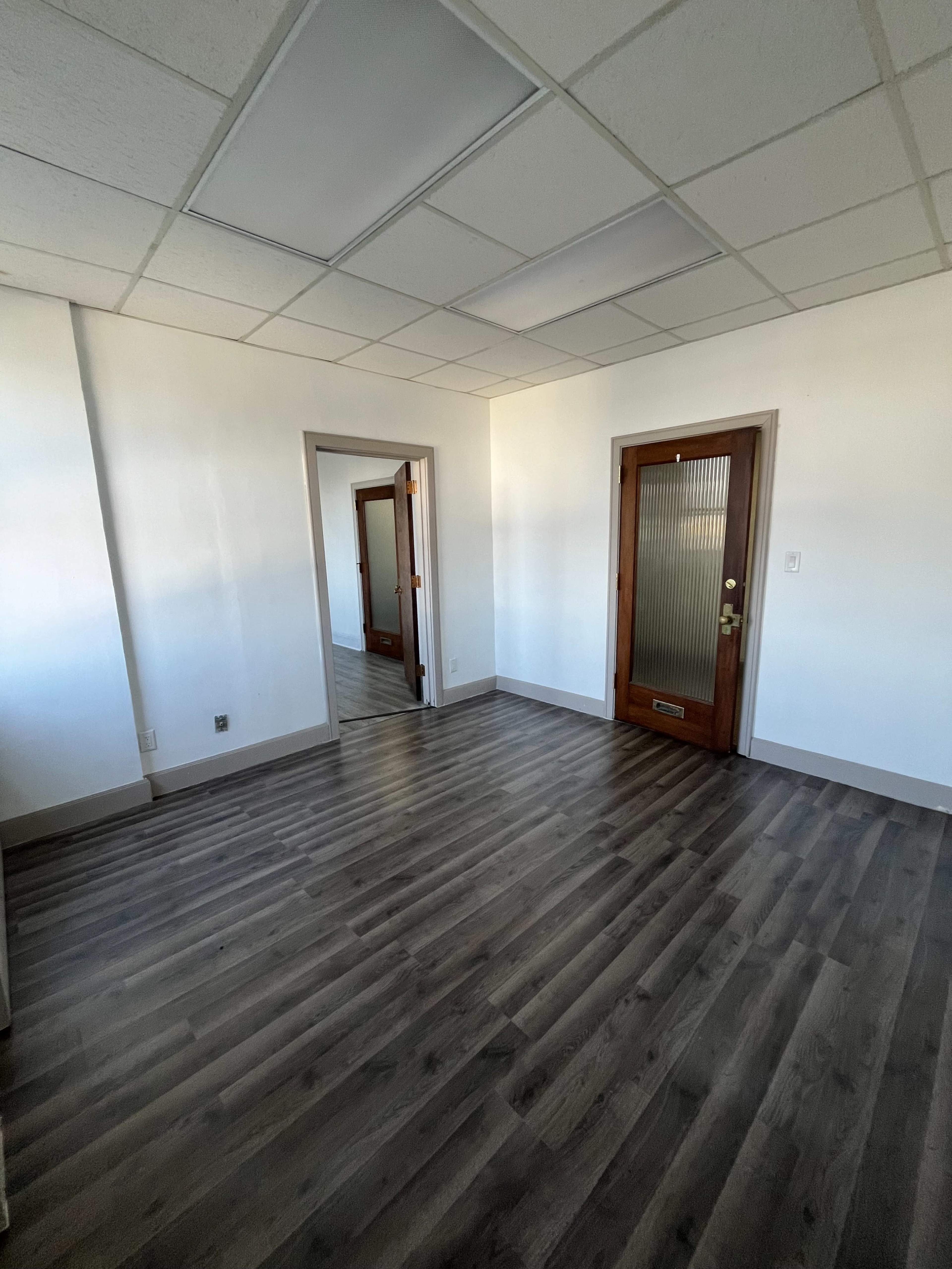 The image shows an empty room with light-colored walls, a wooden door, and a mirrored closet space.