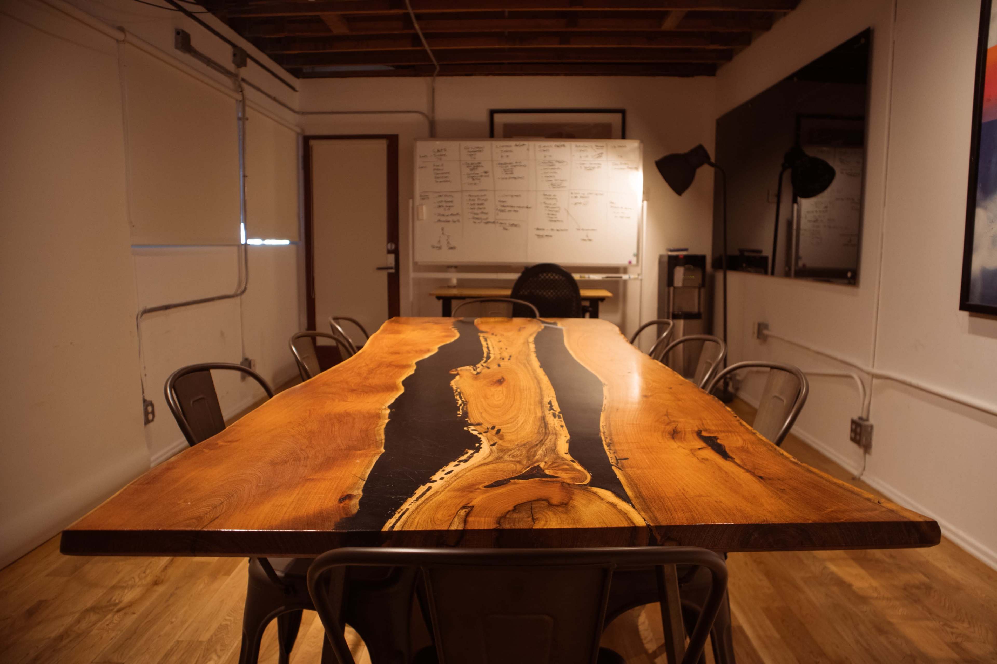 A large wooden conference table with a black resin inlay is surrounded by metal chairs in a well-lit meeting room.
