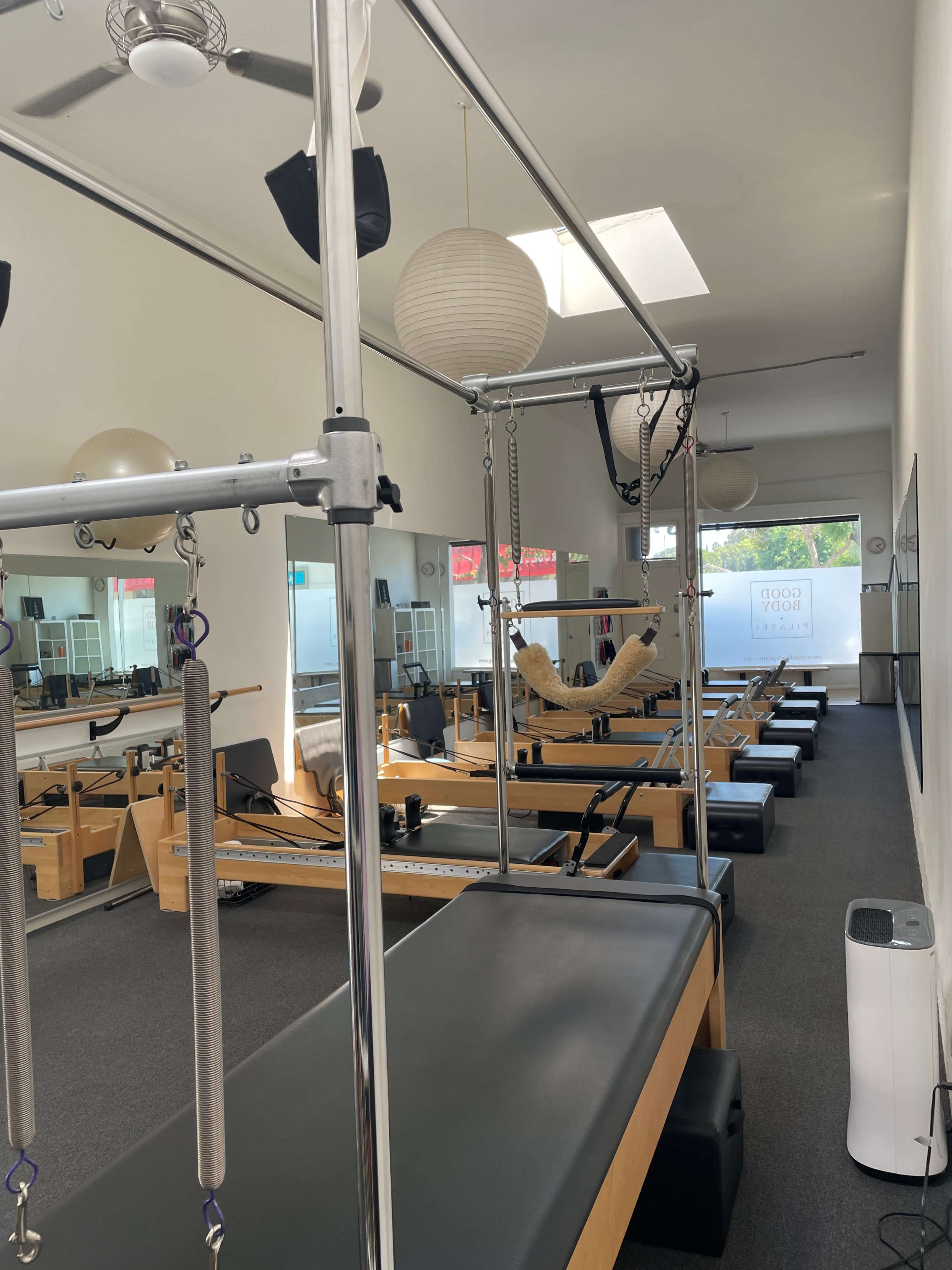 A pilates studio with several reformer machines arranged in rows, illuminated by natural light coming through a skylight.