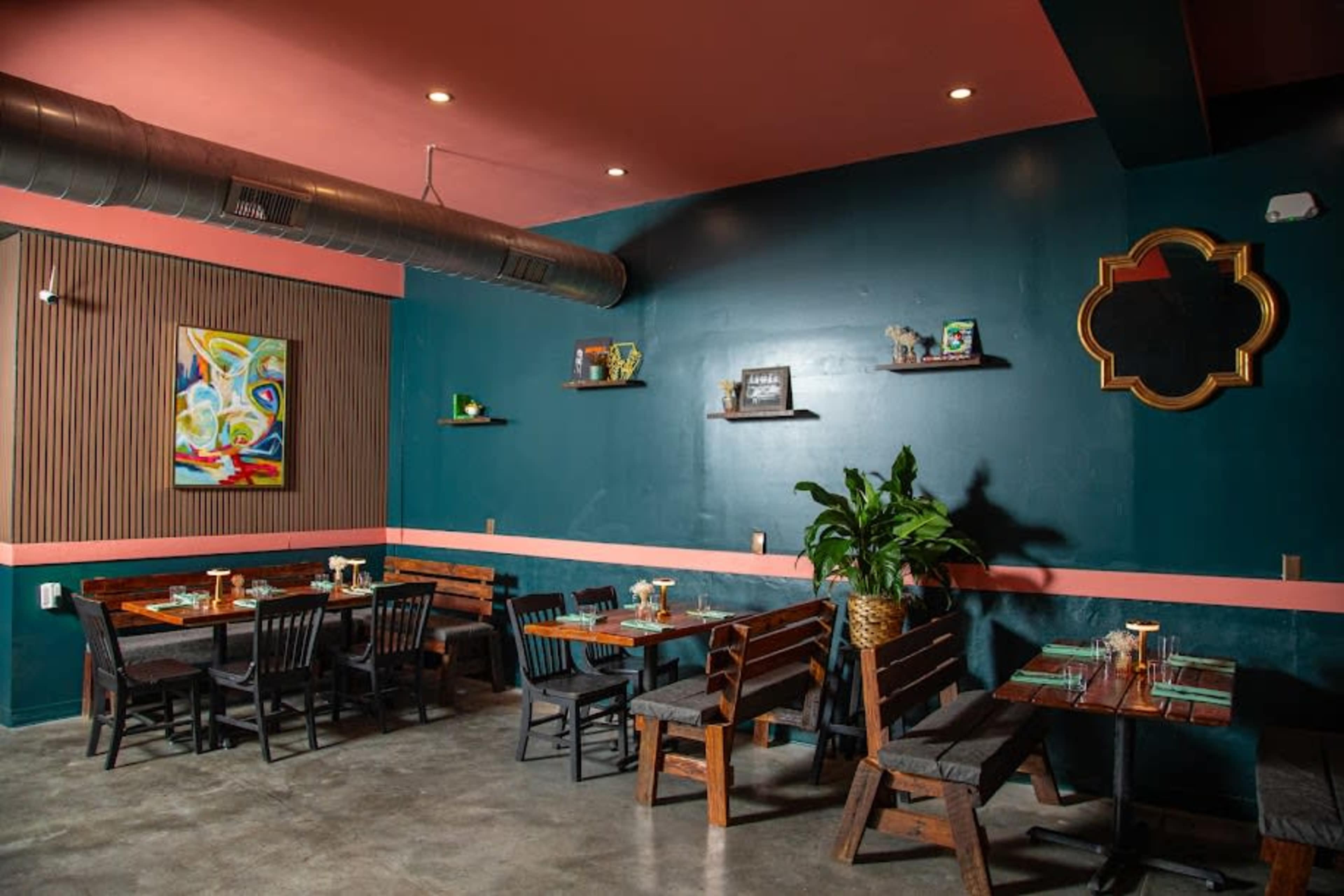 The image features a restaurant interior with dark green walls, wooden tables and benches, and colorful artwork, creating a modern dining space.