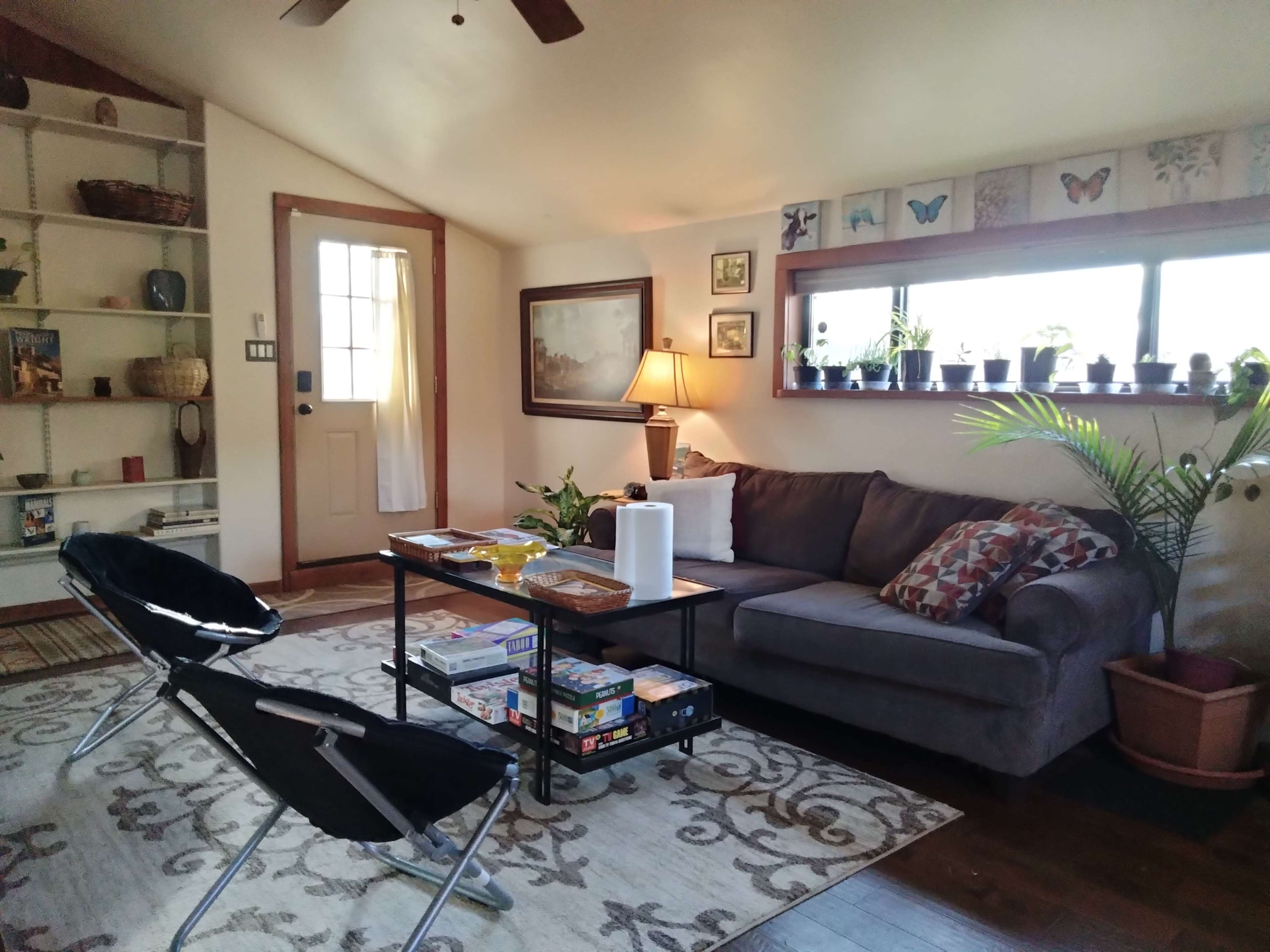 A cozy living room with a sofa, coffee table, books, and plants situated near a door and window.
